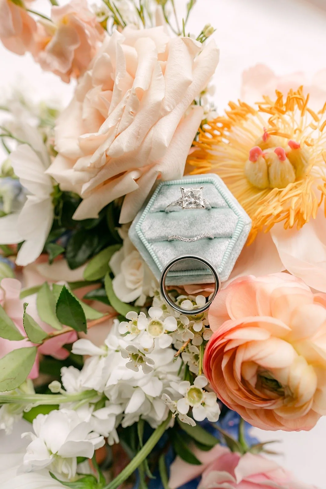 The engagement ring in a blue velvet box tucked into peach and white flowers