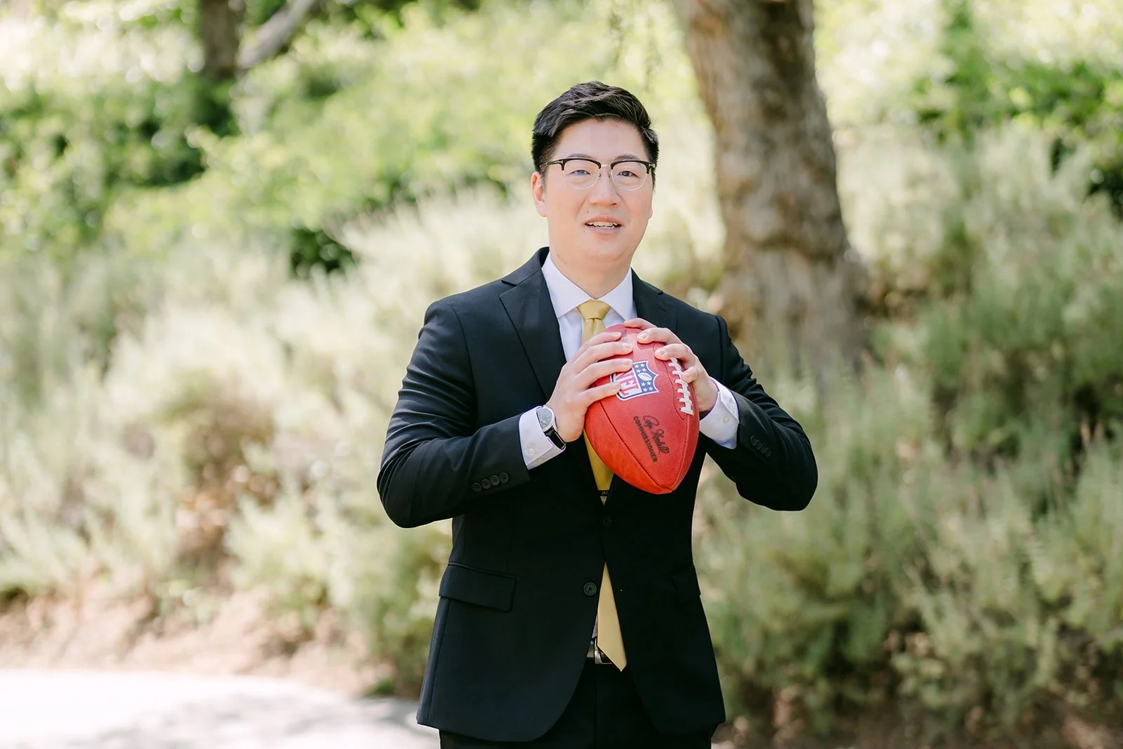 Zach in his black suit and gold tie holding a football in the garden
