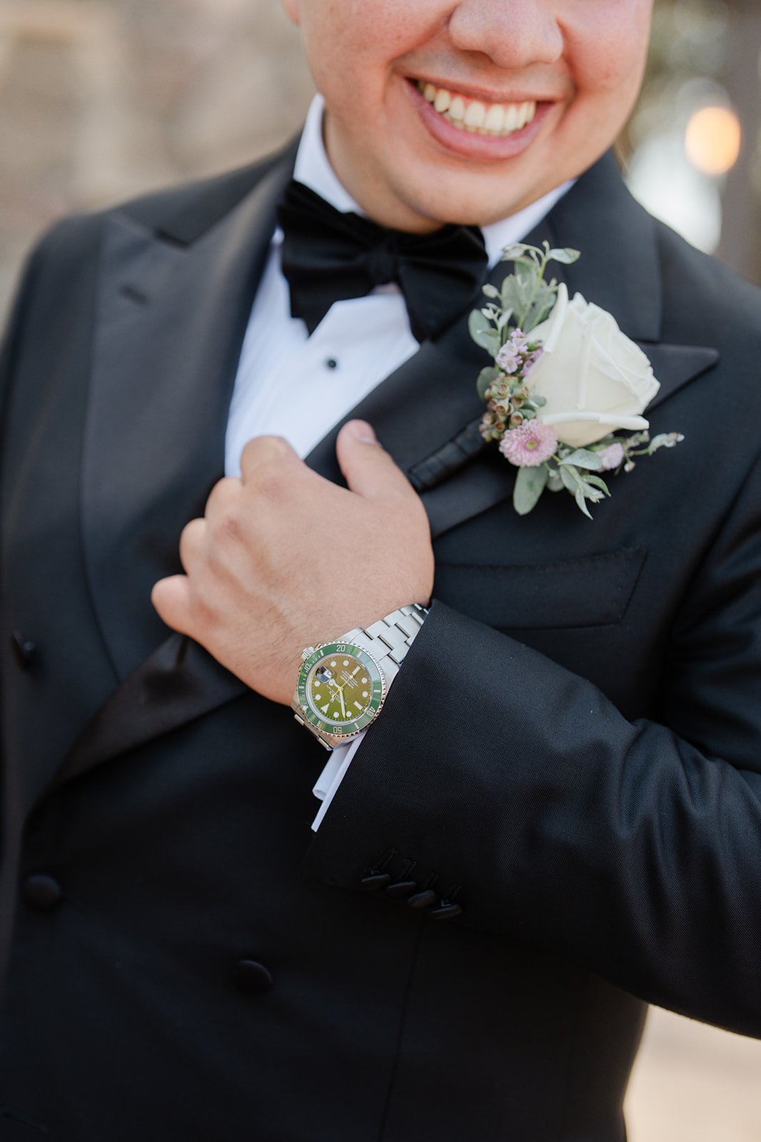 Close up of the groom's smile, watch and white rose boutonniere
