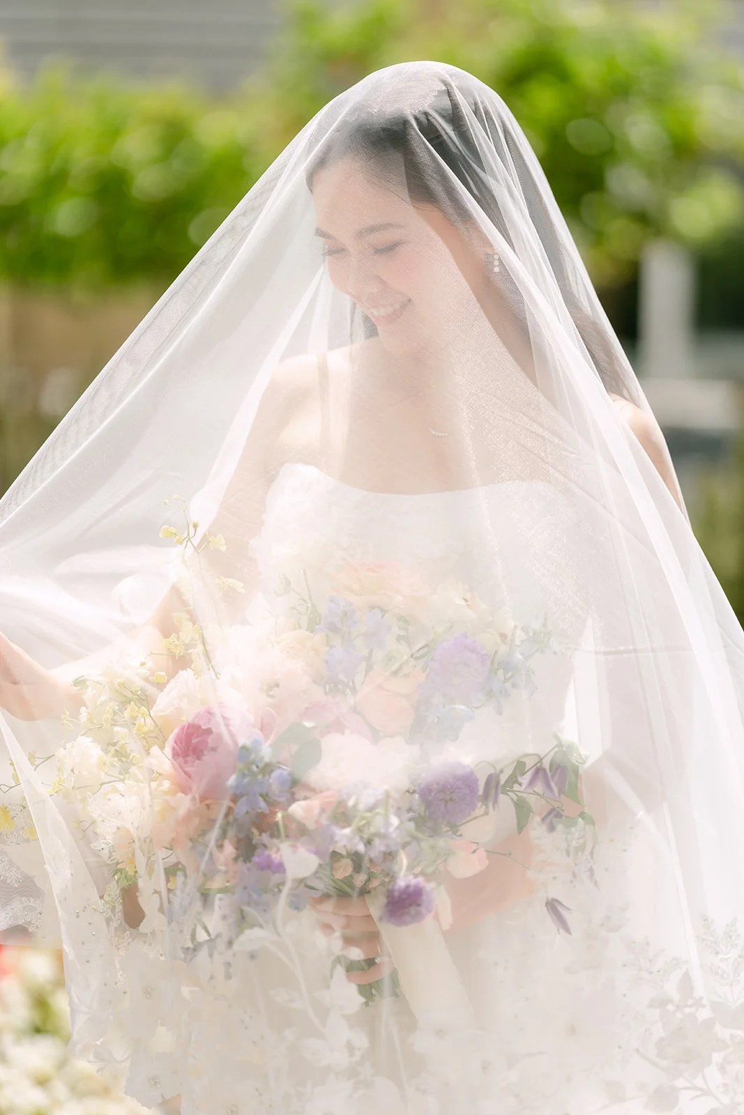 Bride softly framed by her cathedral veil and pastel florals
