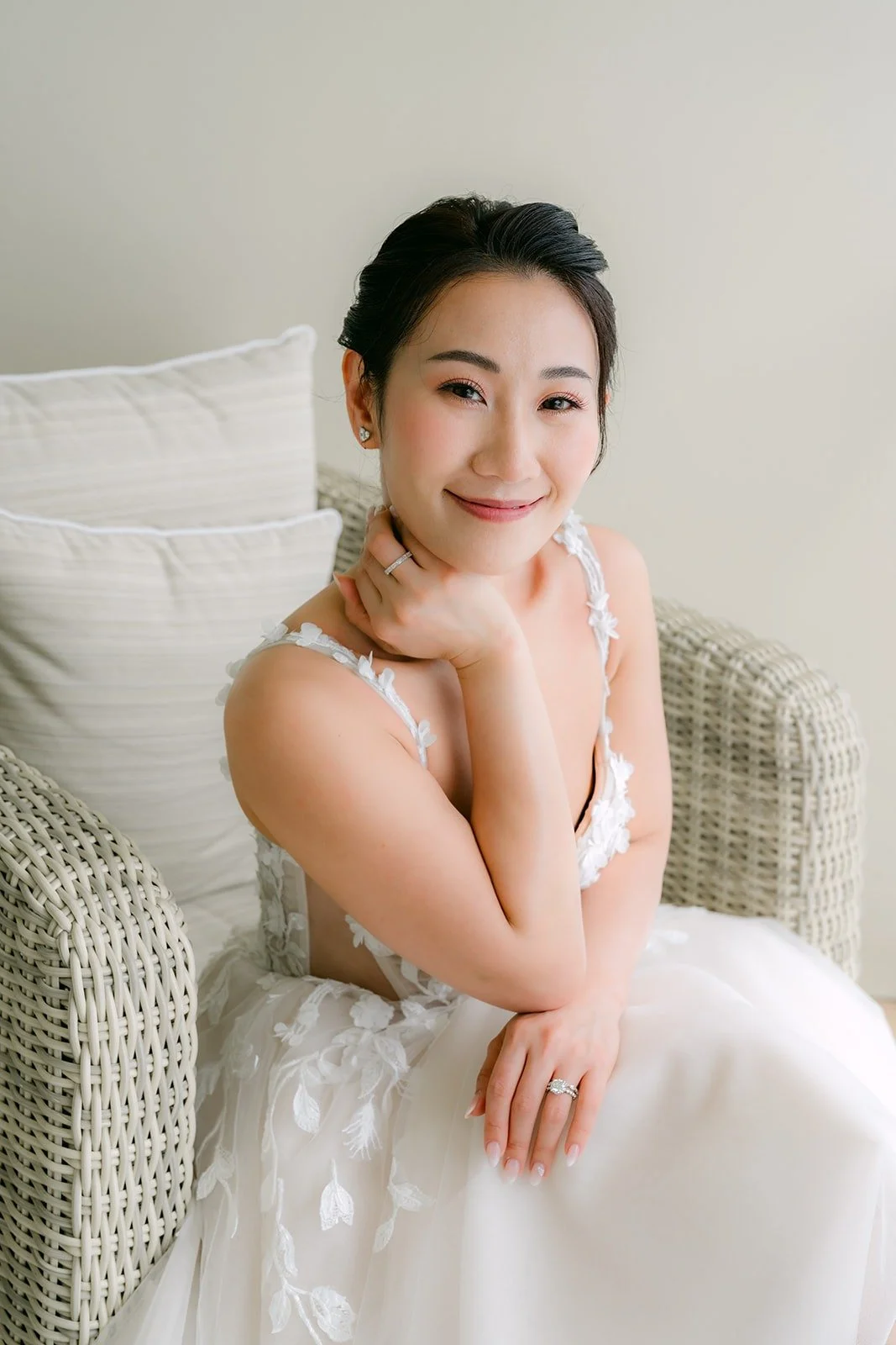 Kylie in her gown sitting in a wicker chair with her hand at her collarbone