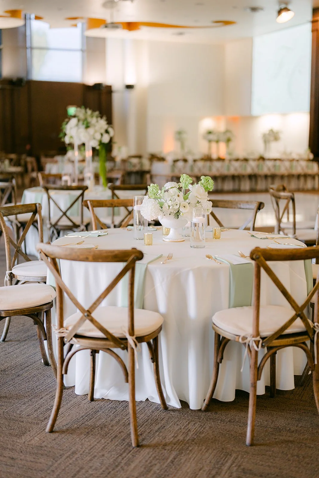 Round tables with wooden cross-back chairs and white florals.