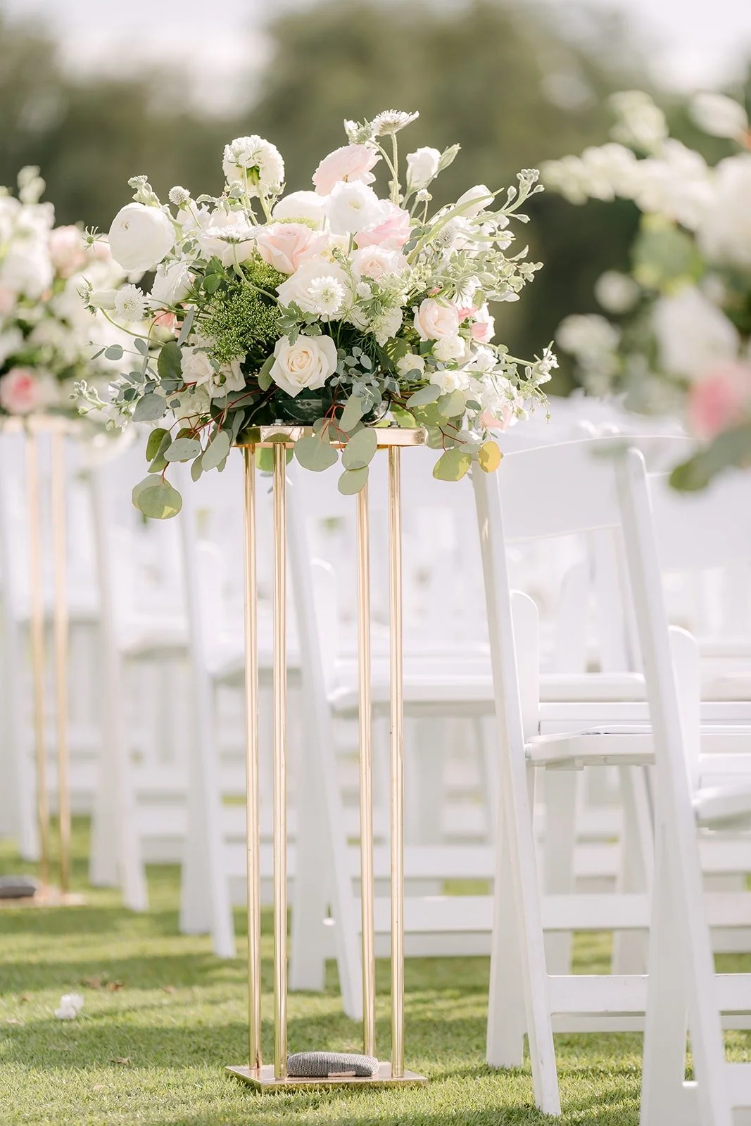 A tall floral arrangement and white chairs on the ceremony lawn