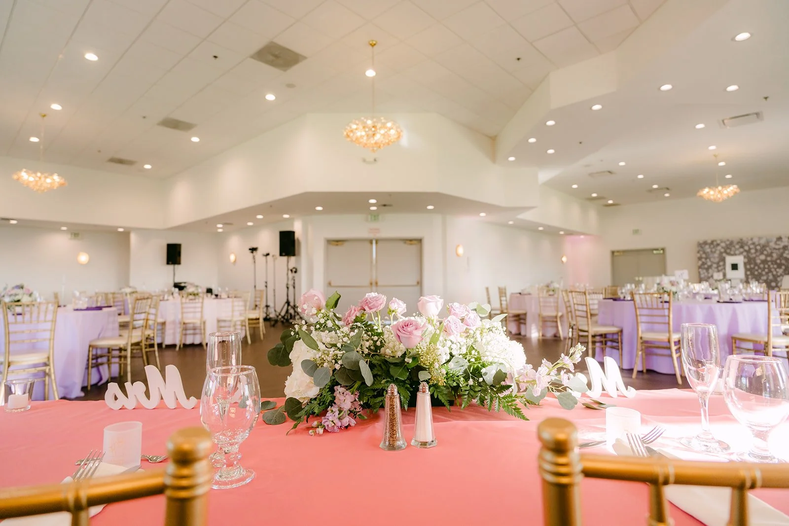 Round tables with blush linens and gold chairs under the arched windows.
