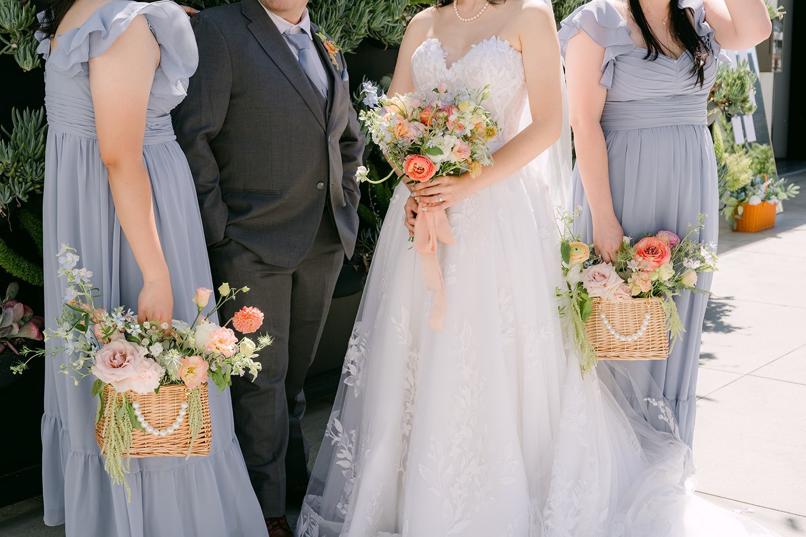 Bridesmaids in dusty blue carrying flower baskets with the bride