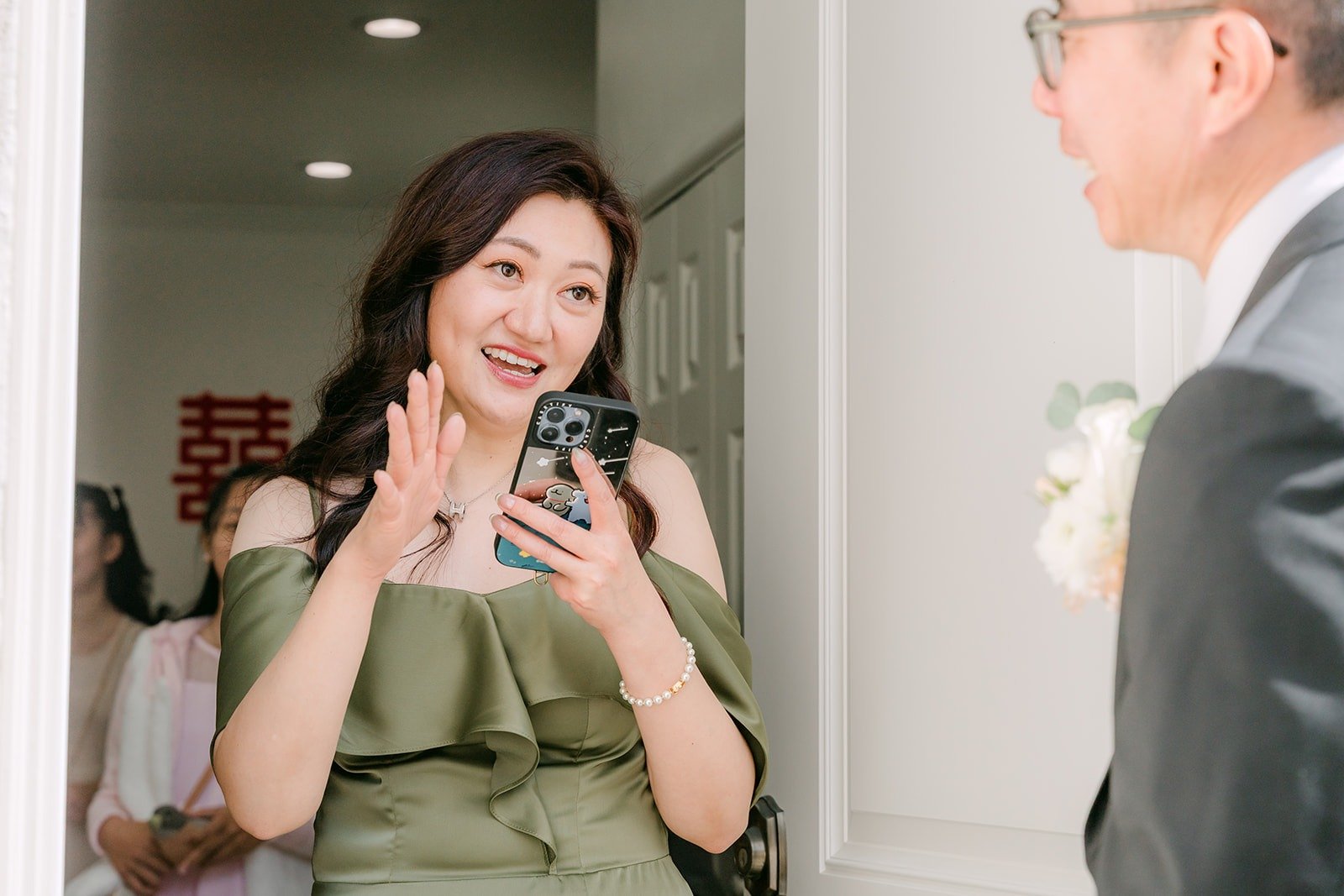 A bridesmaid in olive green grins at the door as the groom's side arrives