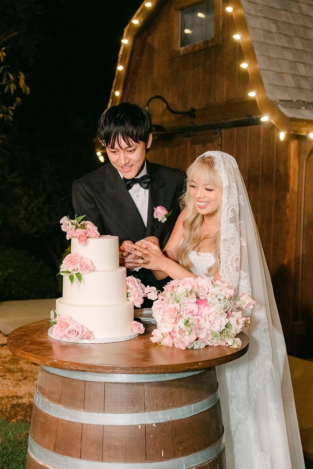 Konitha and Job laughing as they cut the cake on a wine barrel