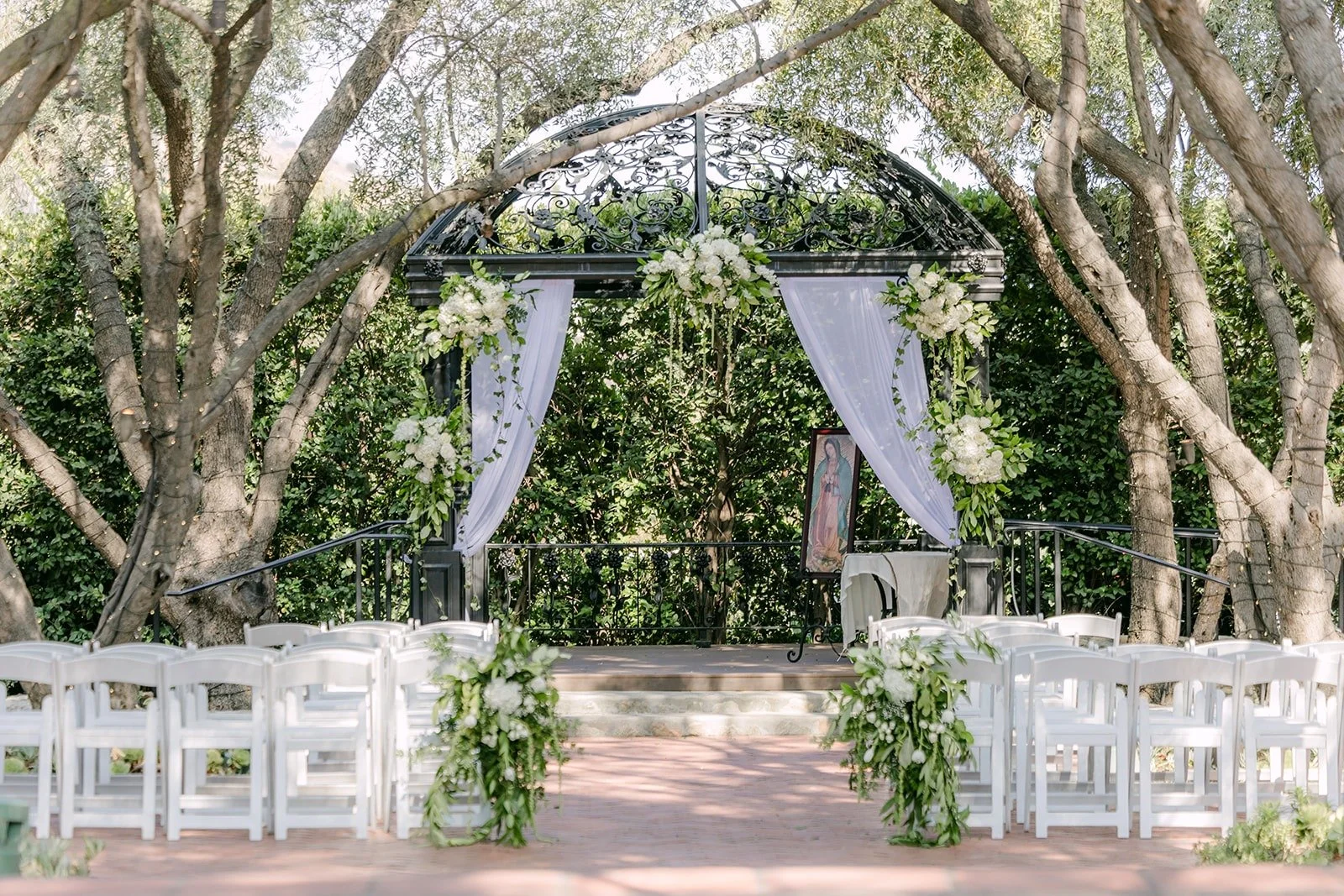 White chairs and greenery lining the aisle toward the wrought iron gazebo at Padua Hills Theatre