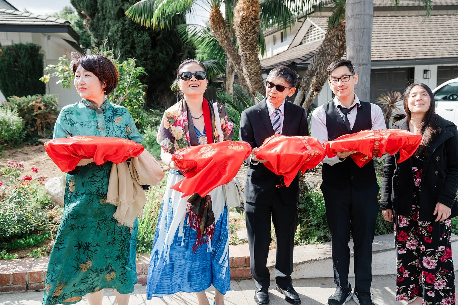 Family members in ao dai and suits holding red gift trays.