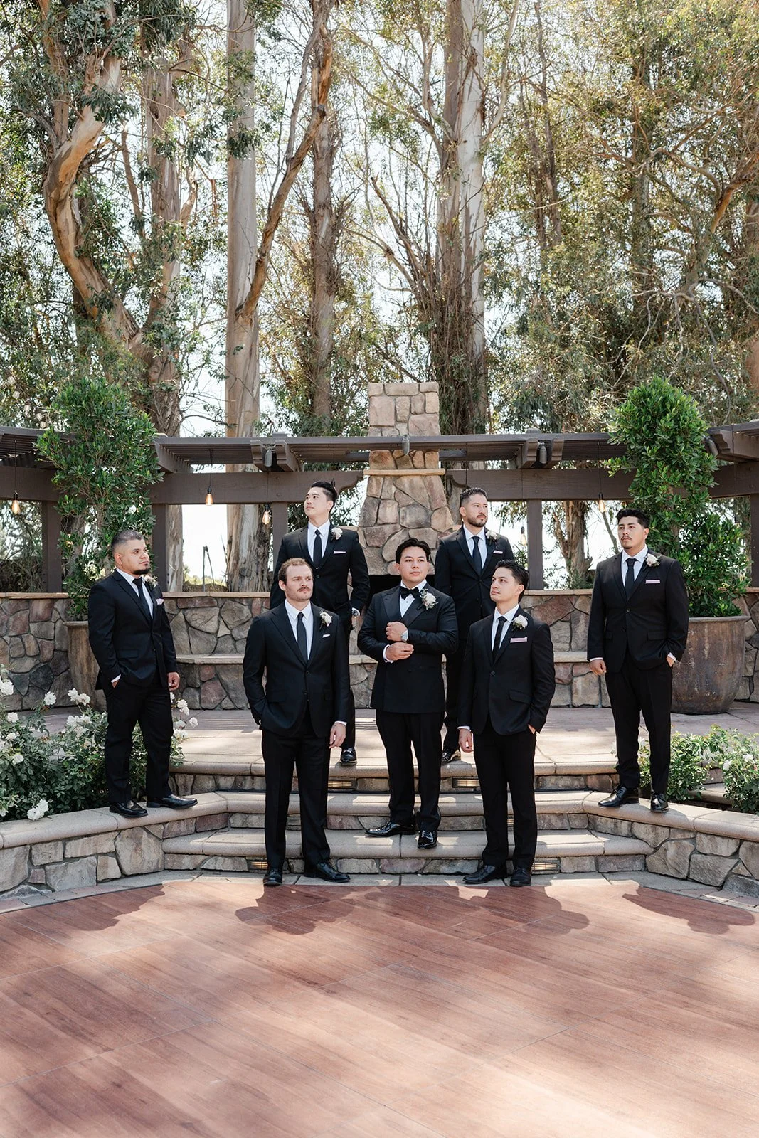 Groom and groomsmen in black tuxedos by the stone fireplace