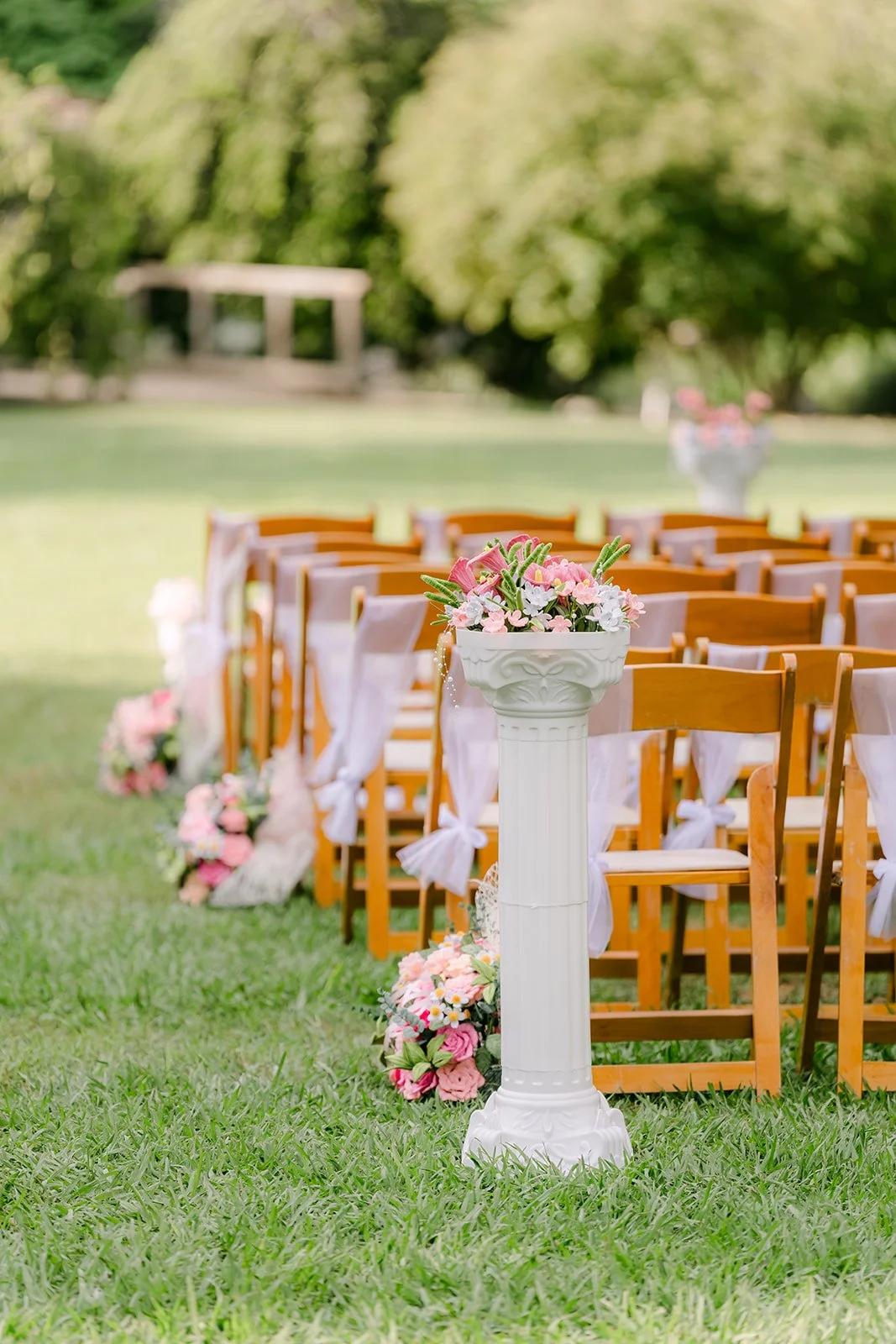 Aisle lined with pink florals on pedestals and wooden chairs.