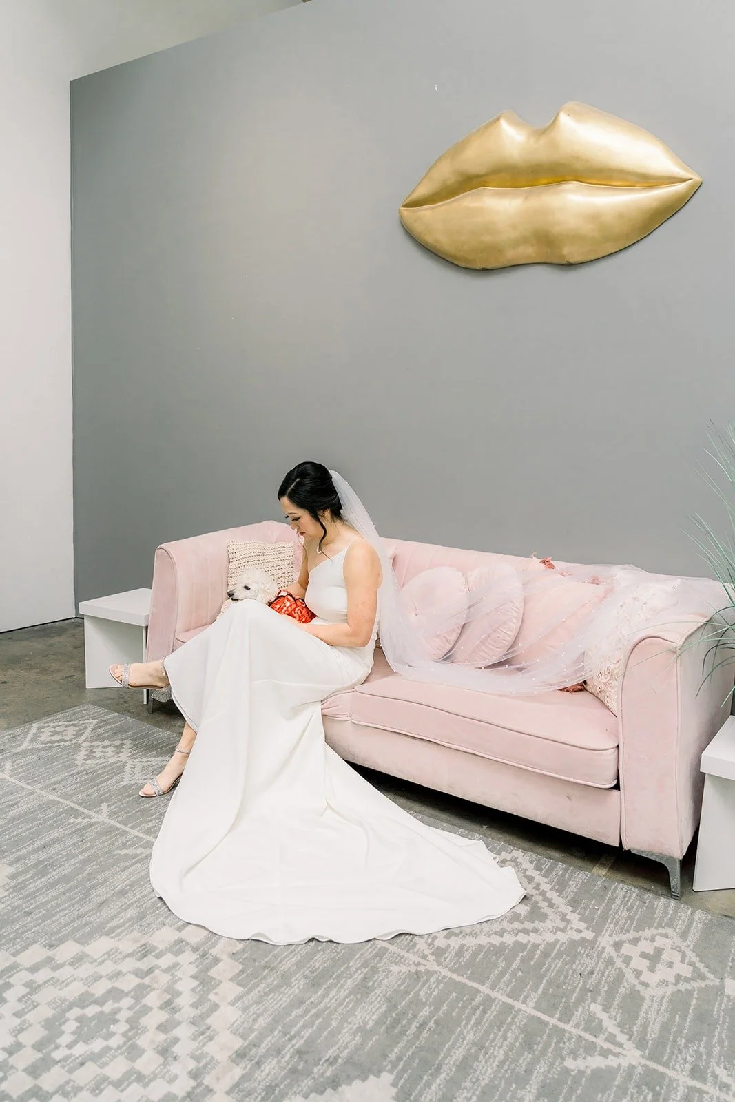 Cindy on a blush pink sofa beneath a gold lips wall sculpture
