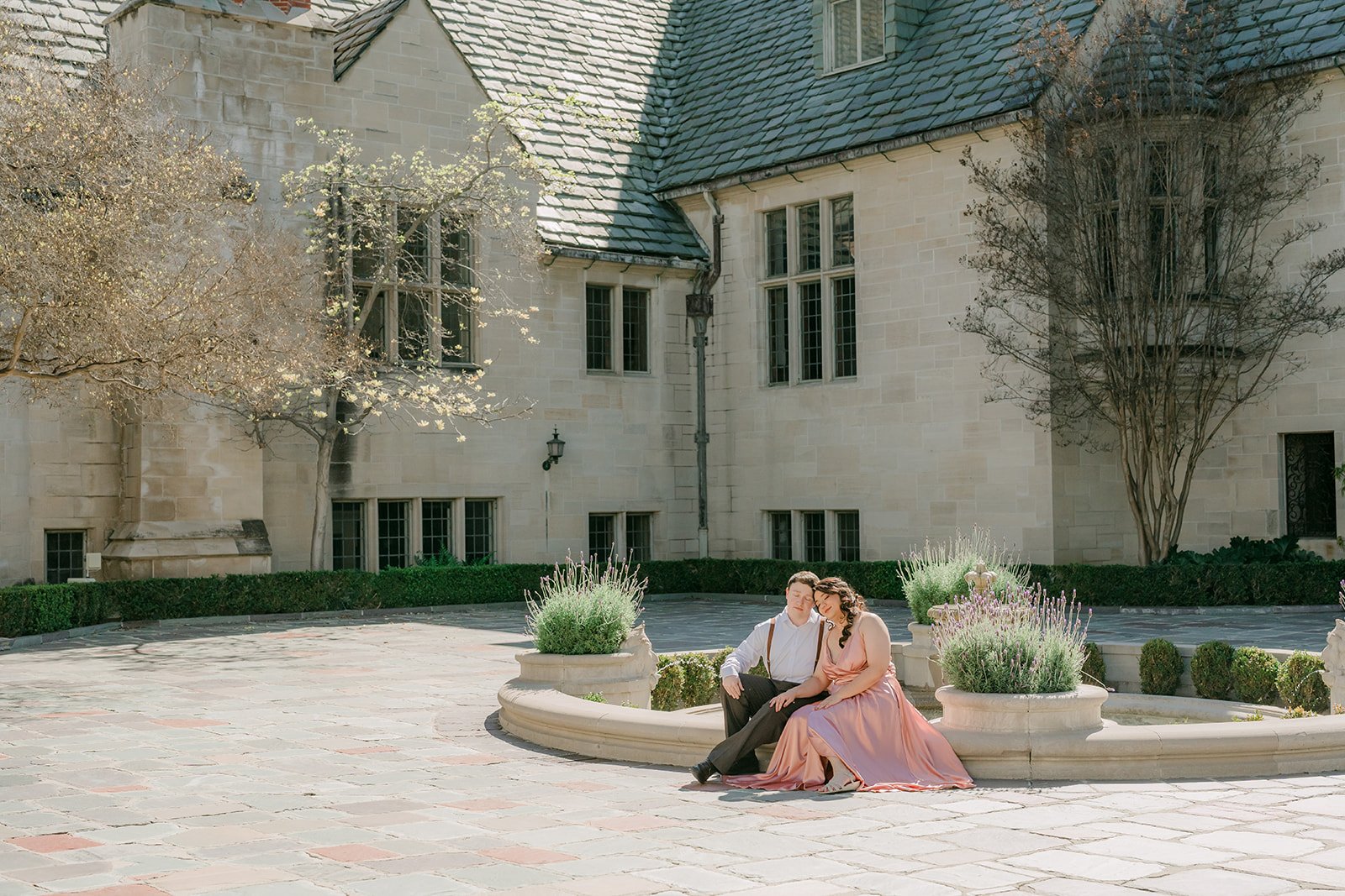 The couple at the fountain with the mansion's slate roof and chimneys behind them.