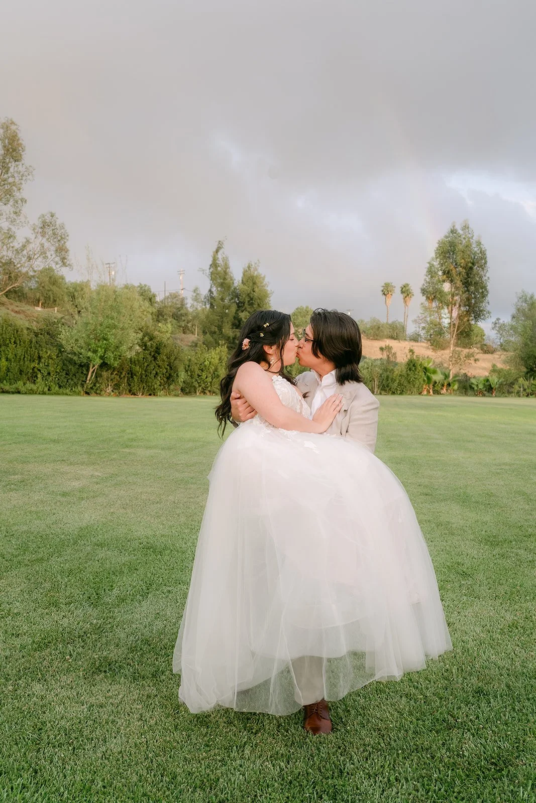 Bride and groom sharing a kiss on the lawn at dusk, photographed by One and Only Production