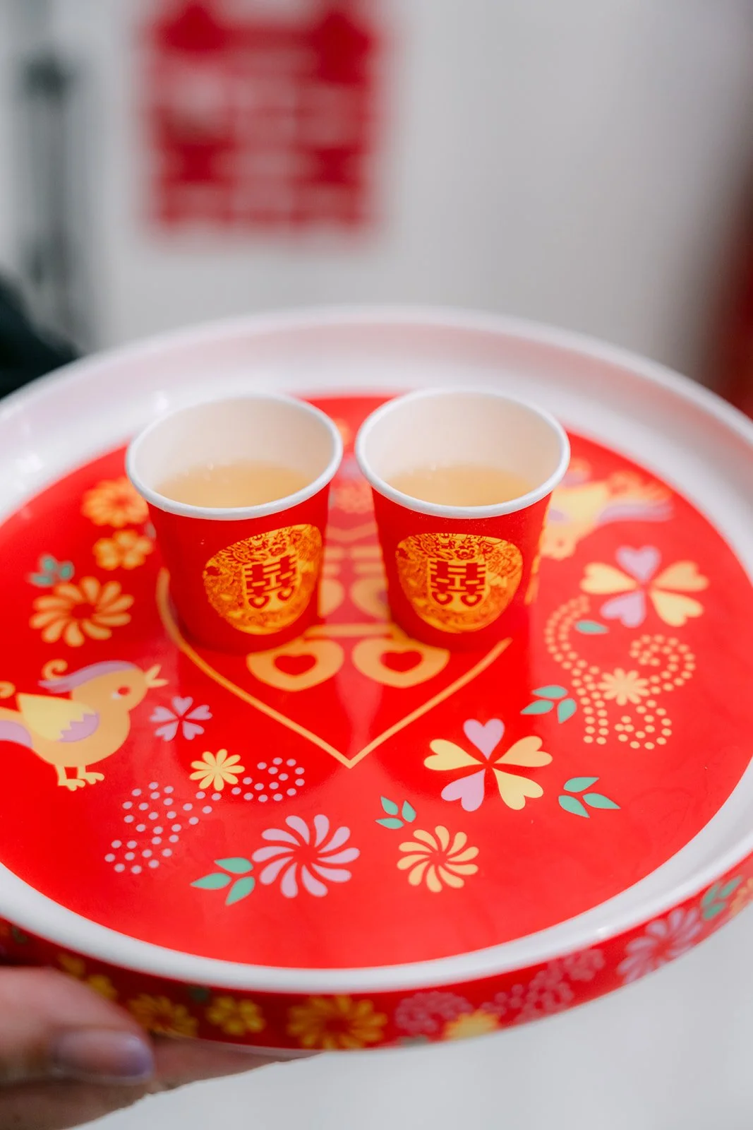 Two teacups filled with tea on a red tray before serving.