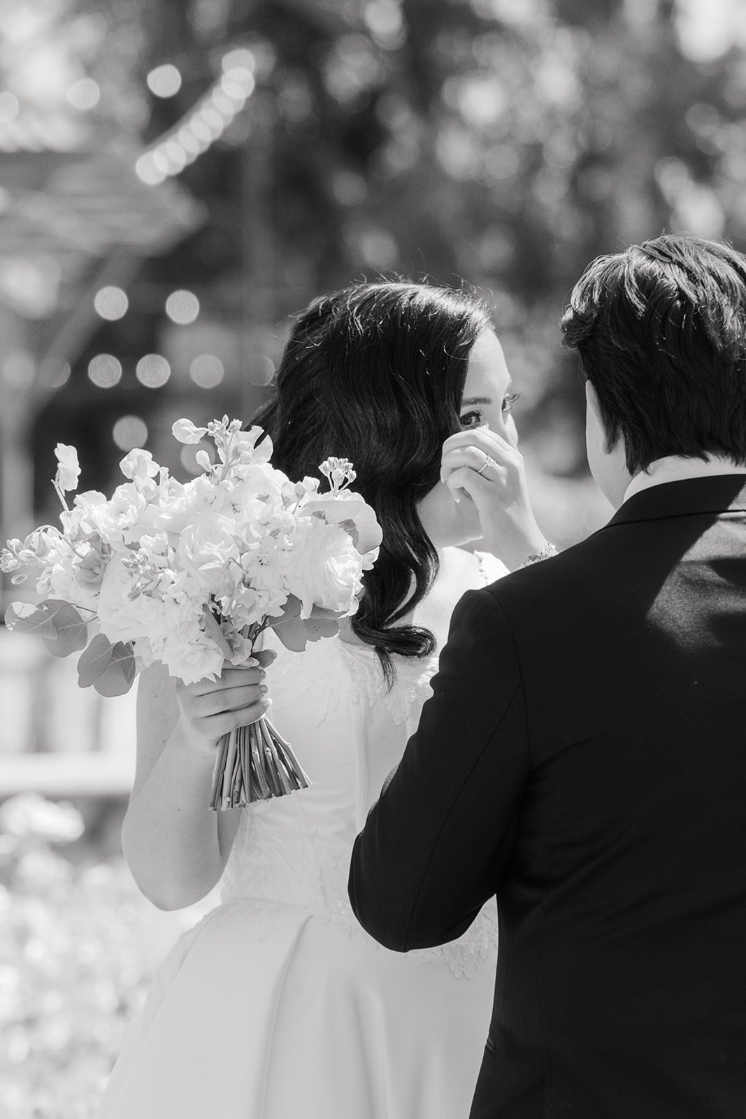 Black and white photo of the bride wiping a tear during the vows