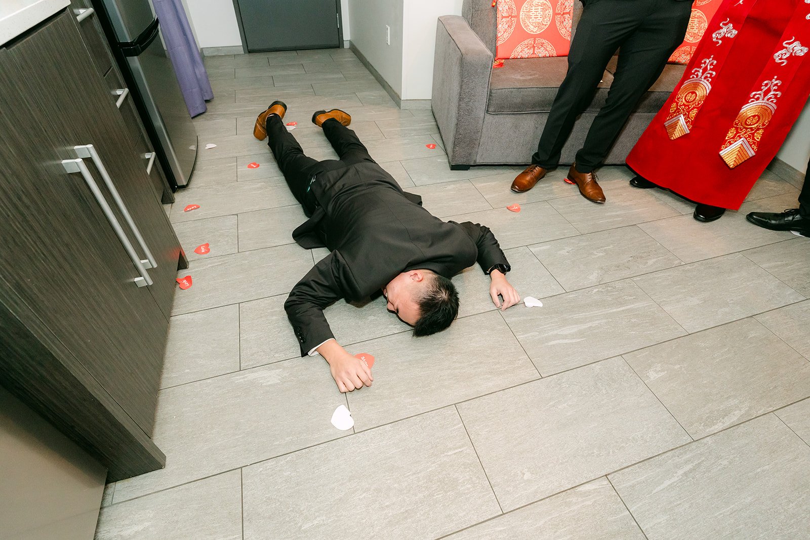 A groomsman lying flat on the hallway floor during a door game challenge.