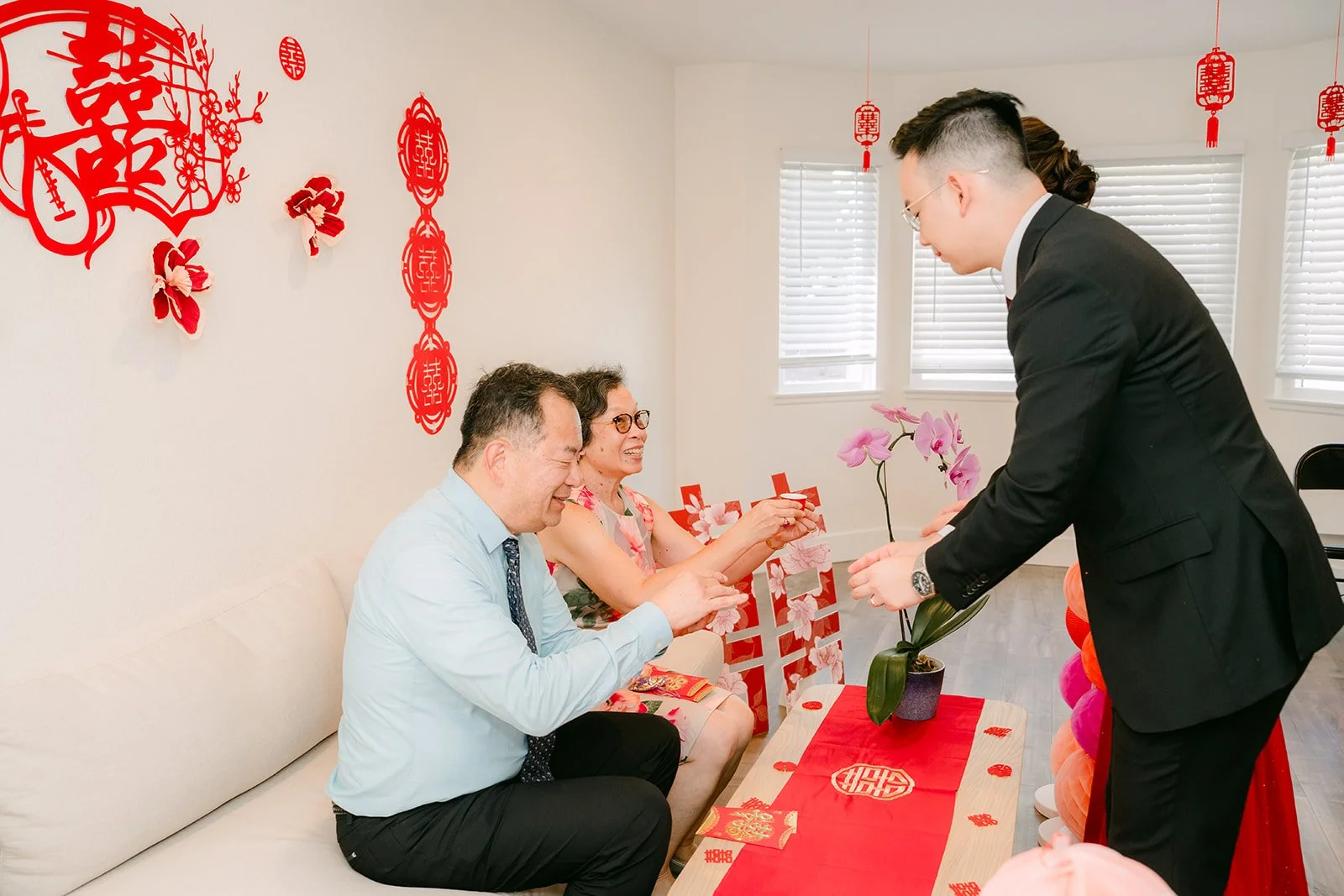 Ken's family looking on as the couple serves tea.
