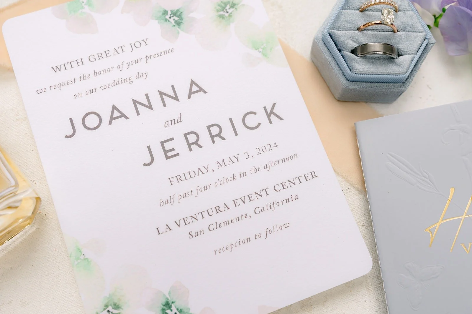 Joanna and Jerrick's invitation with a dusty blue ring box and lavender sweet peas