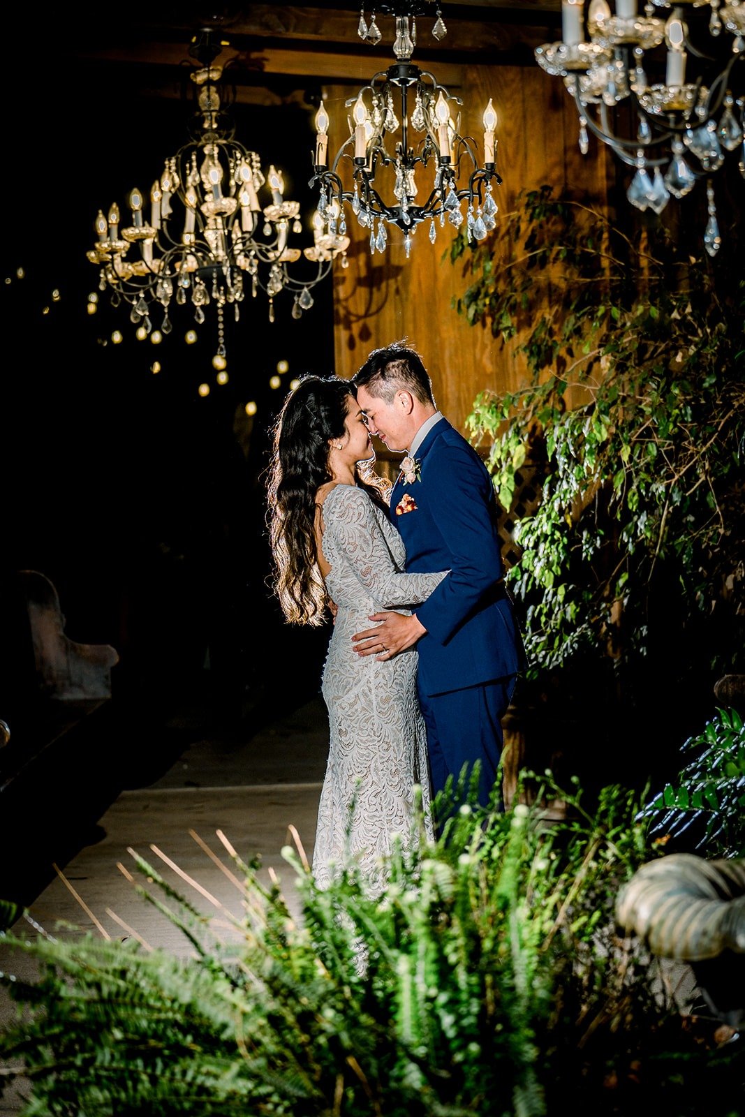 Hannah and Vincent kissing beneath chandeliers in the garden at night, photographed by One and Only Production