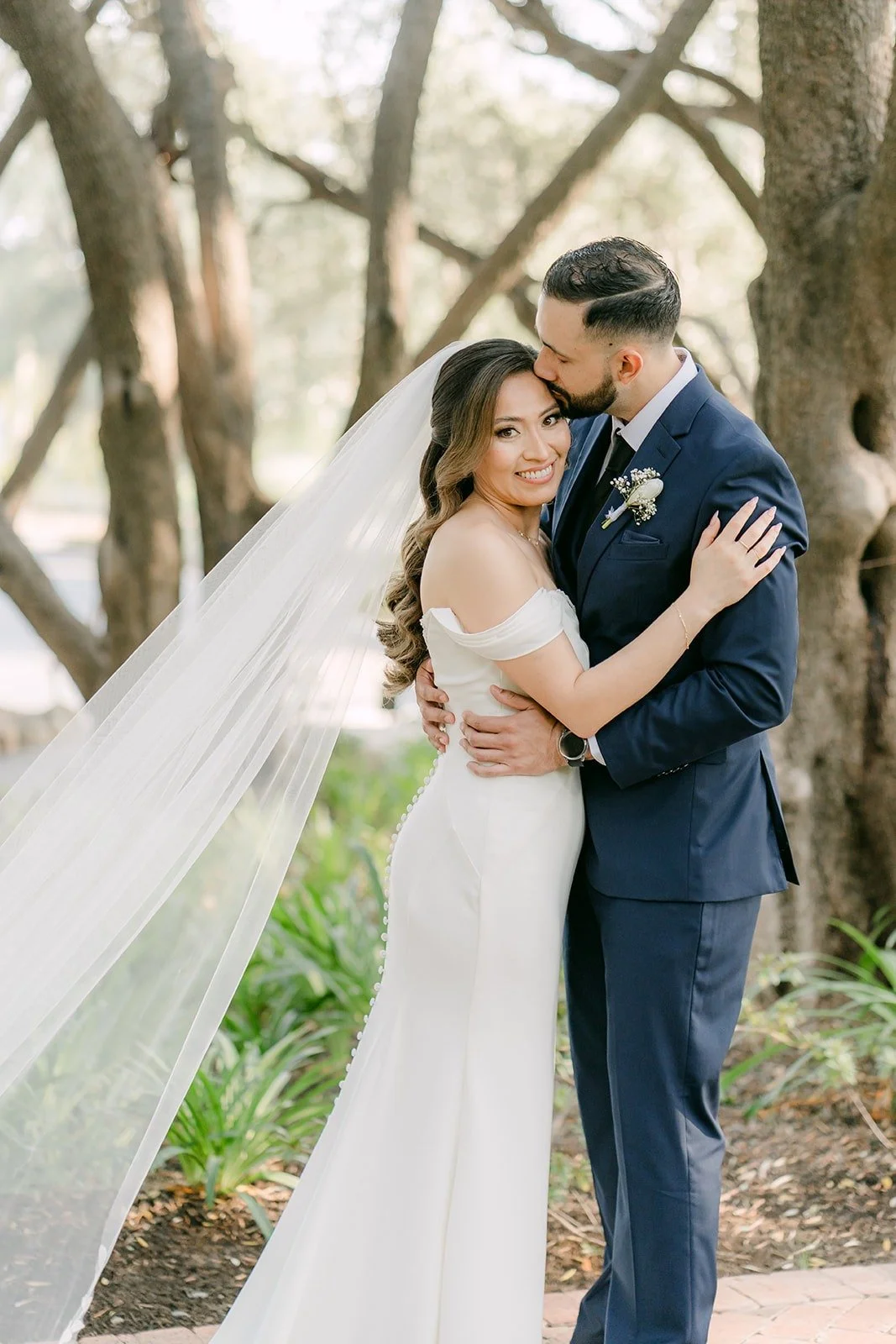 Mariana and Danny embracing under the trees as Danny kisses her forehead