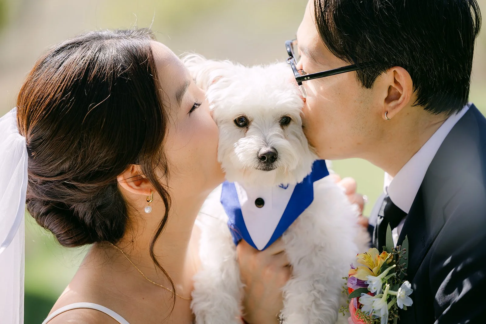 Saya and Leroy kissing their pup Soup in his tuxedo bandana
