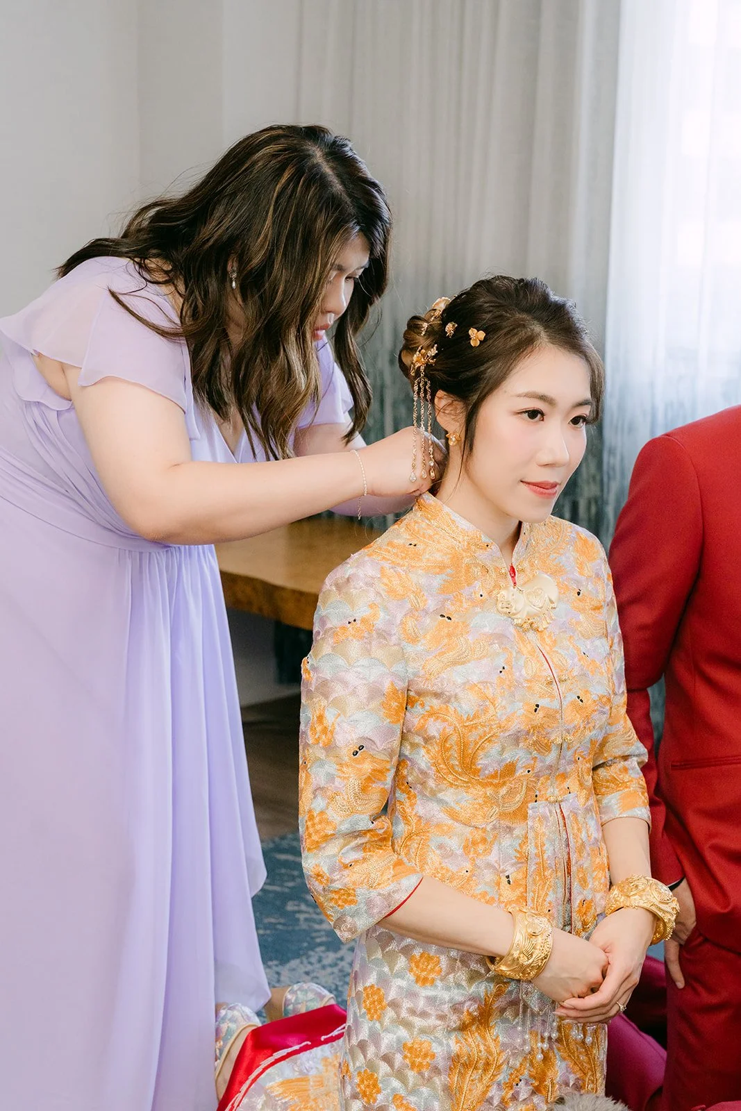 A bridesmaid fastens a gold necklace on Christie during the tea ceremony.