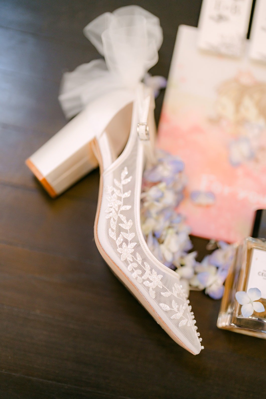 A beaded lace block heel next to a white bow and pink stationery