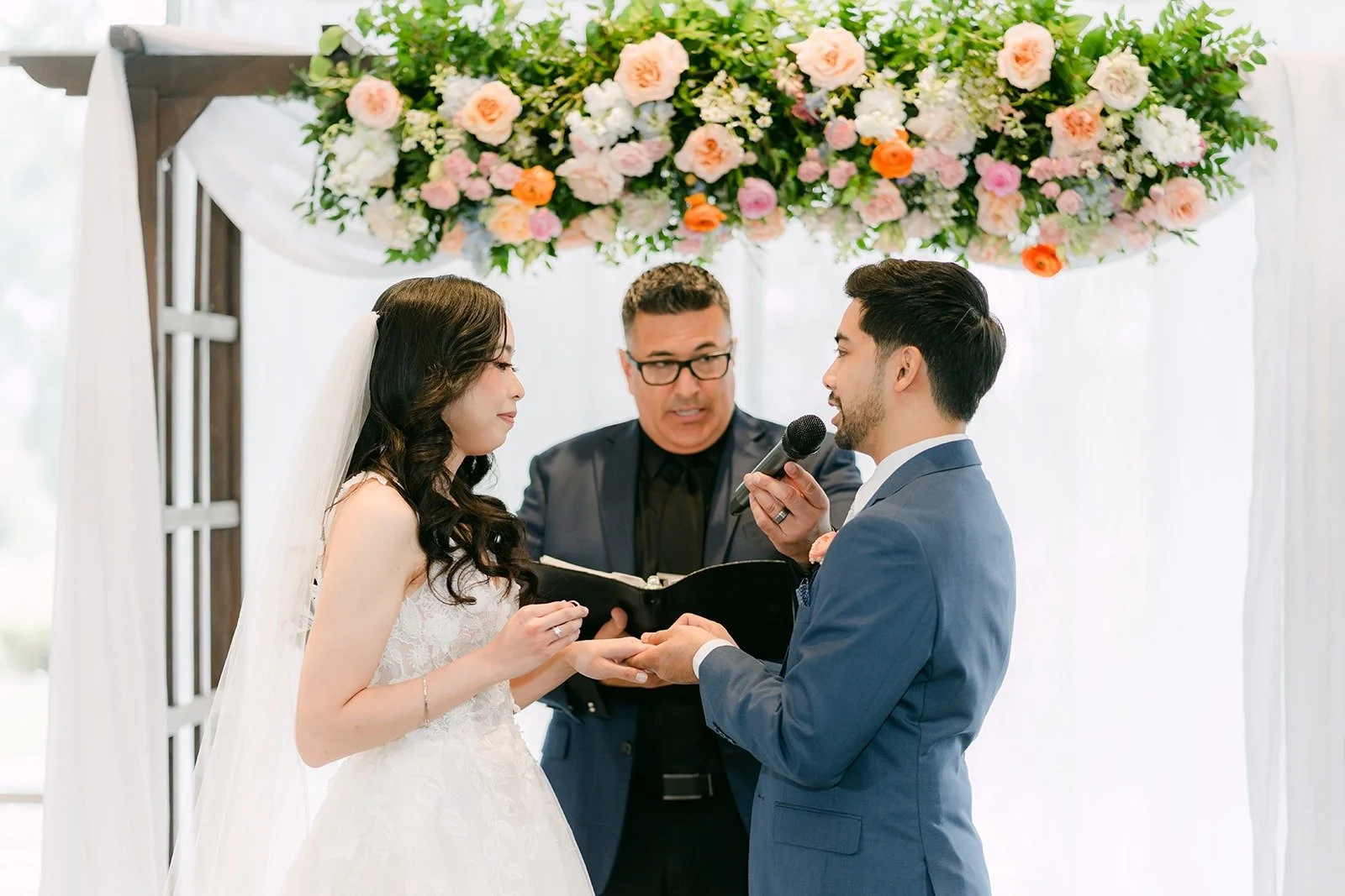 Natalie and Mark exchanging rings as officiant Joe Rivera holds the microphone