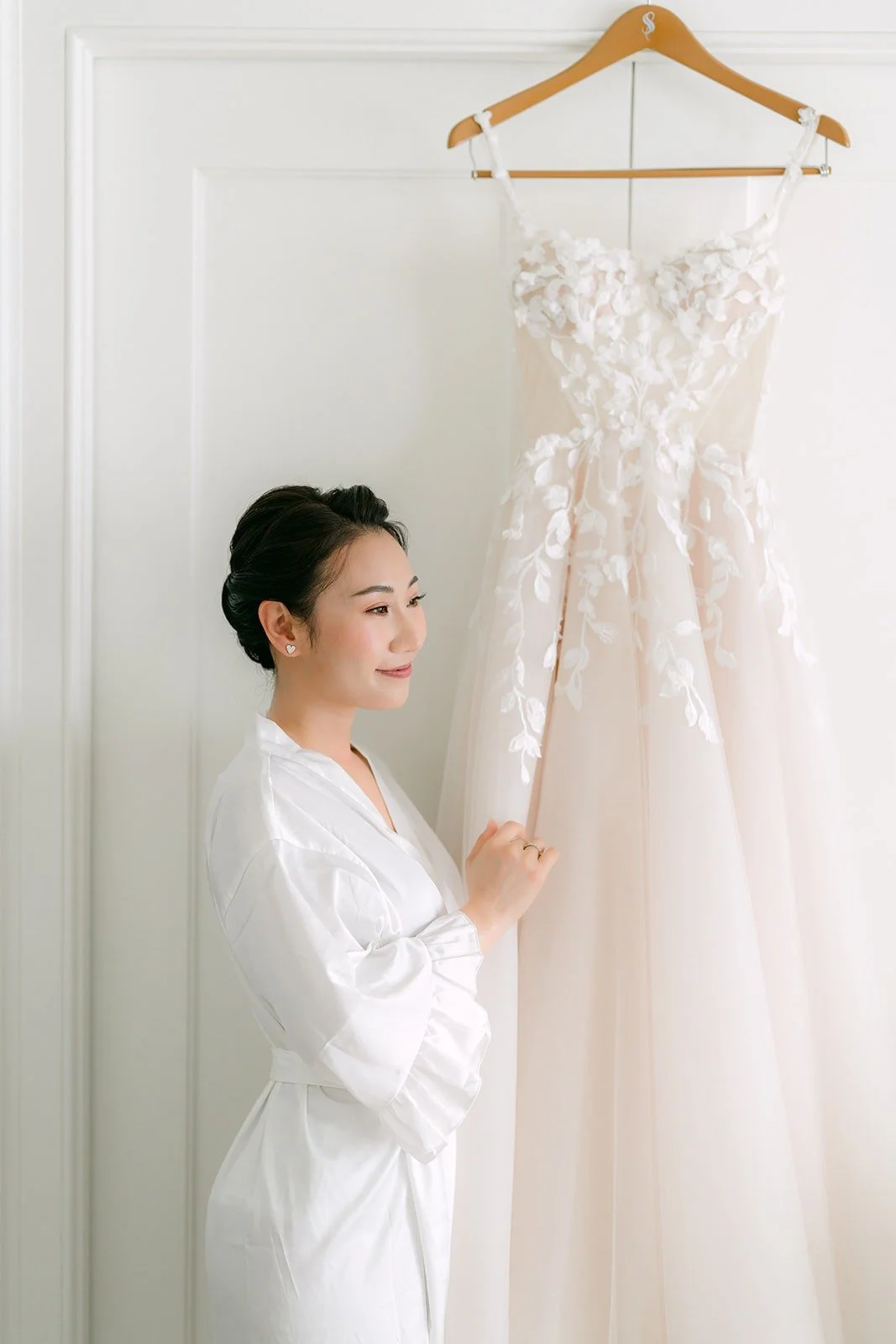 Kylie in a white robe looking up at her gown on its hanger
