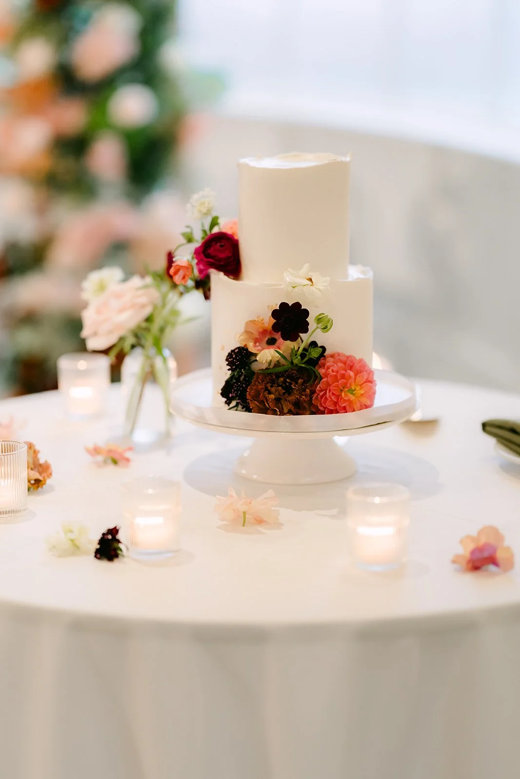 Two-tier white wedding cake with burgundy and peach florals.