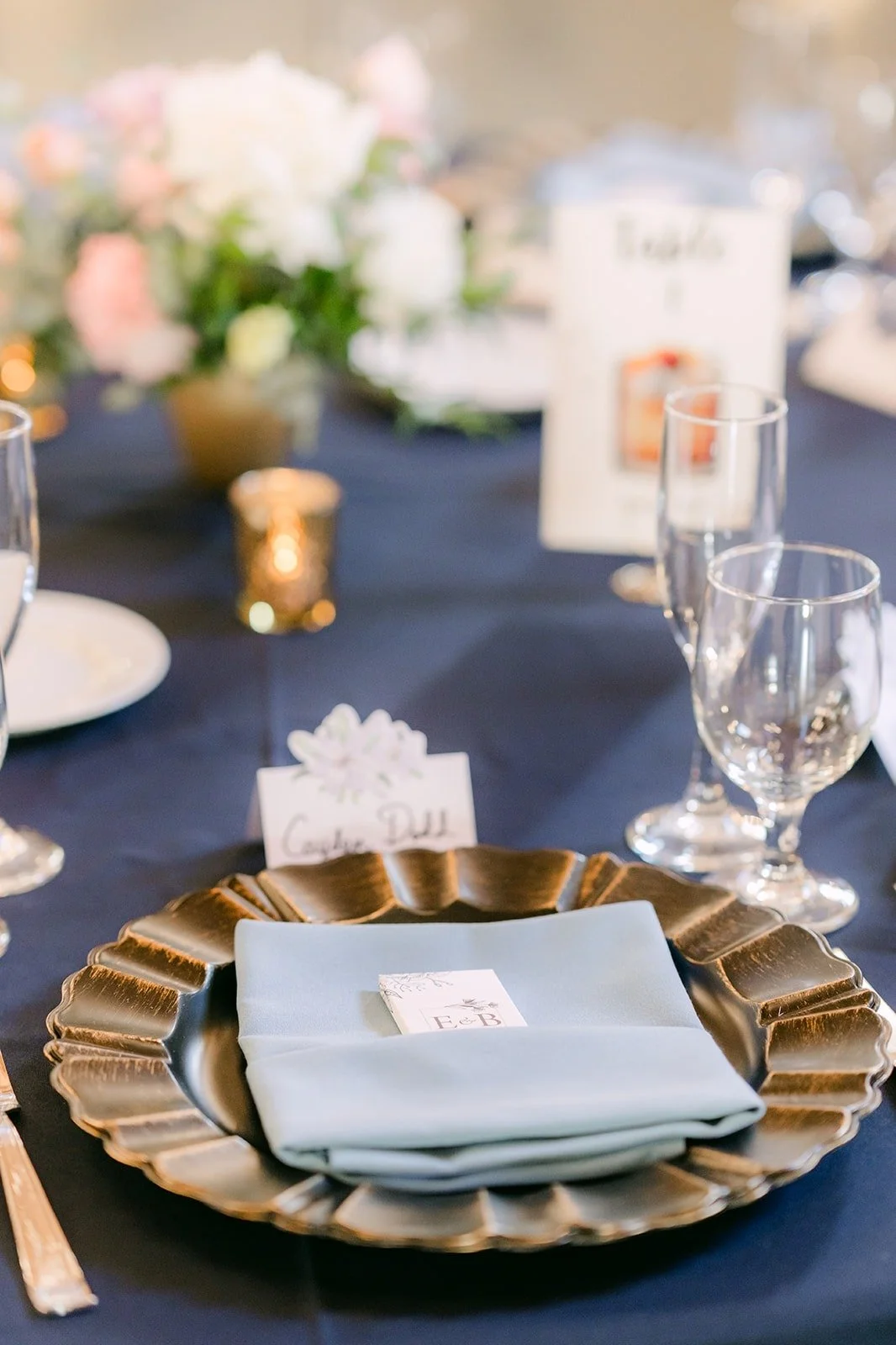 A place setting with a gold charger and a pale blue napkin on a navy tablecloth