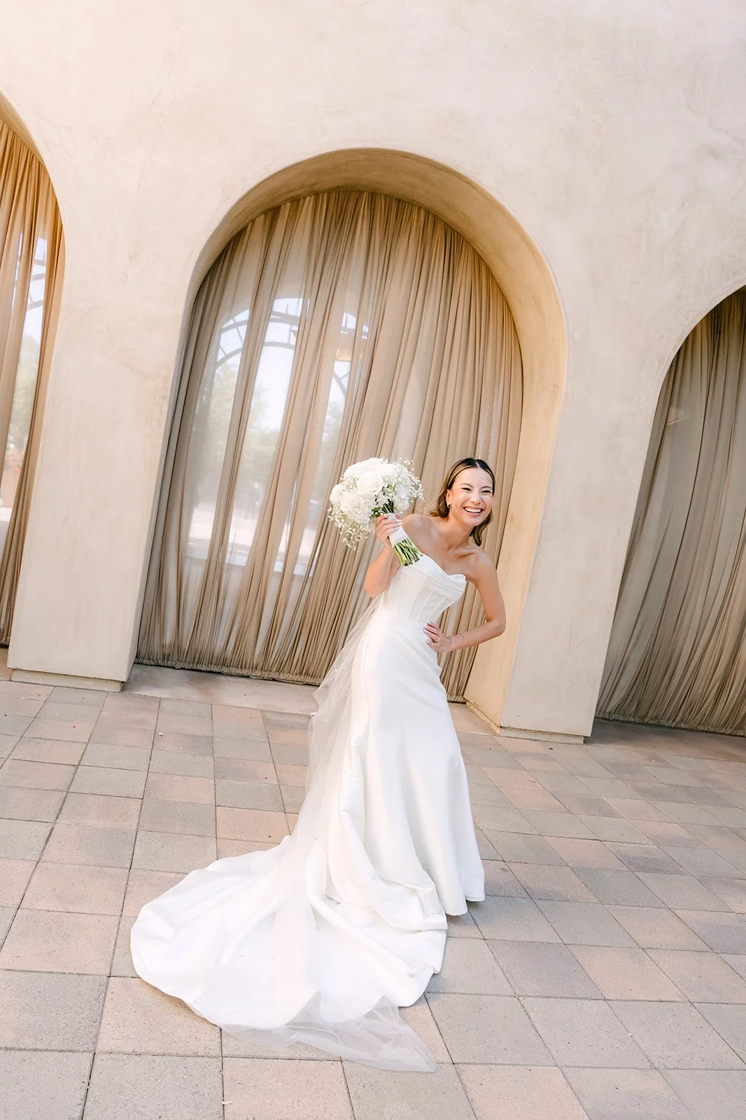 Bride raising her bouquet in celebration under the arches