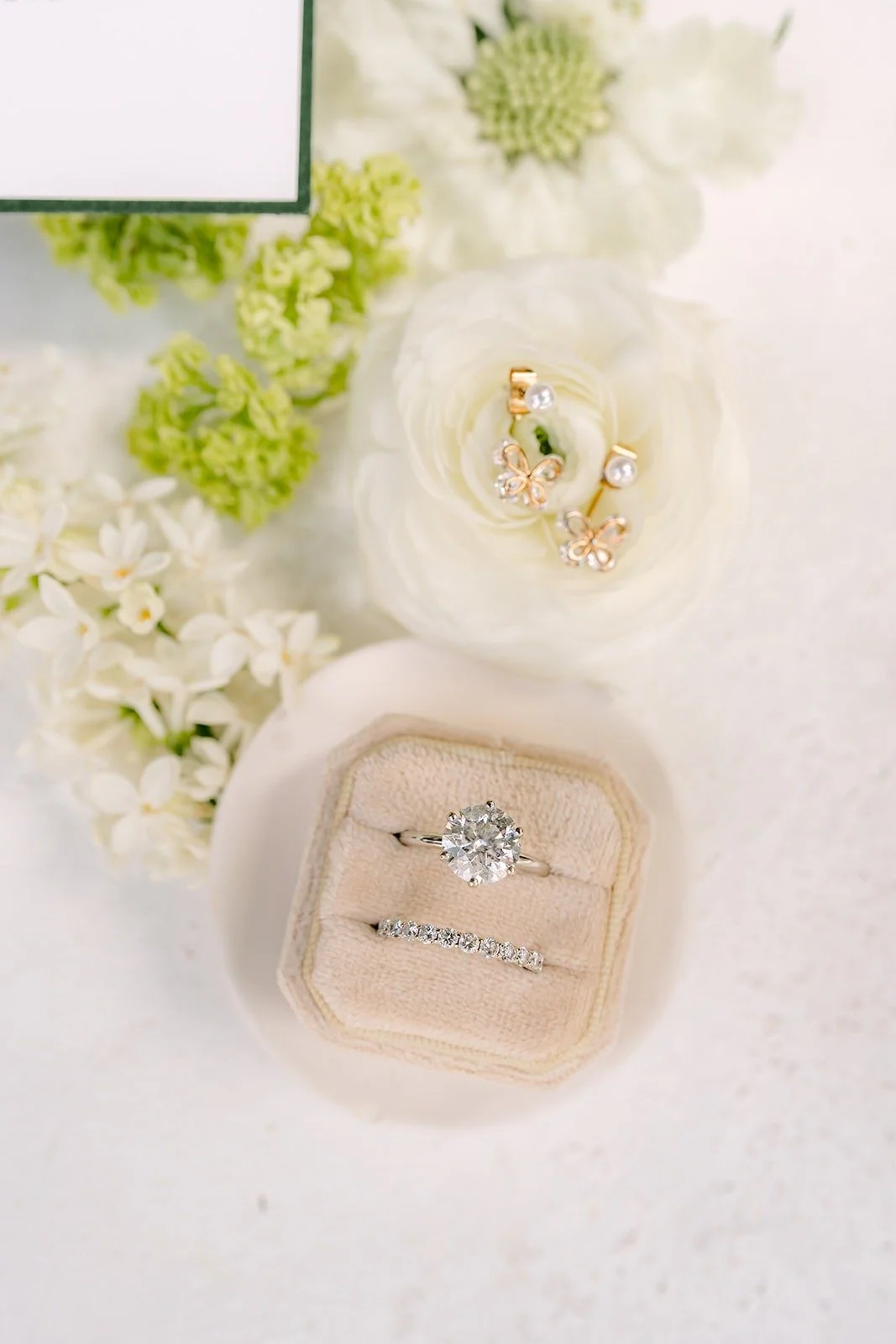 A cream ring box holding the engagement ring among soft white blooms
