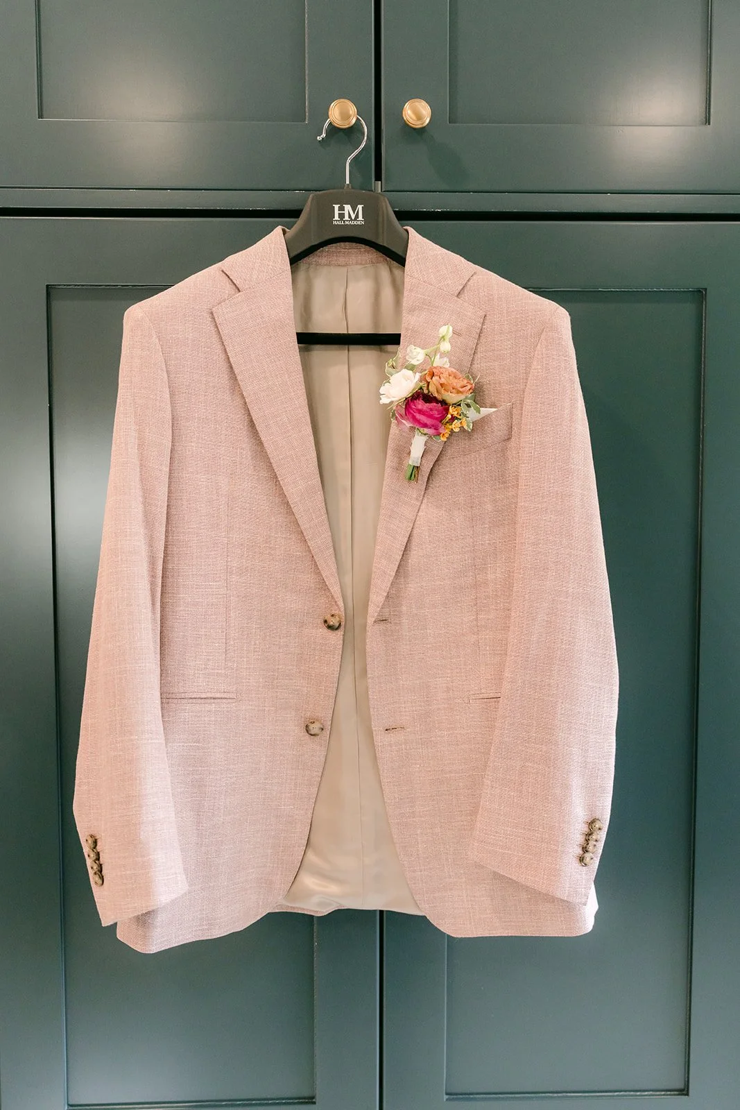Michael's blush suit jacket hanging on a green cabinet with his boutonniere pinned on.
