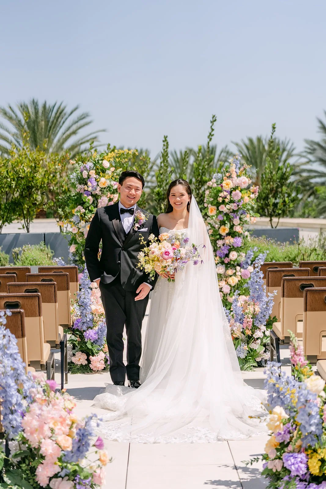 Linh and Hoan standing together at the top of their floral ceremony aisle