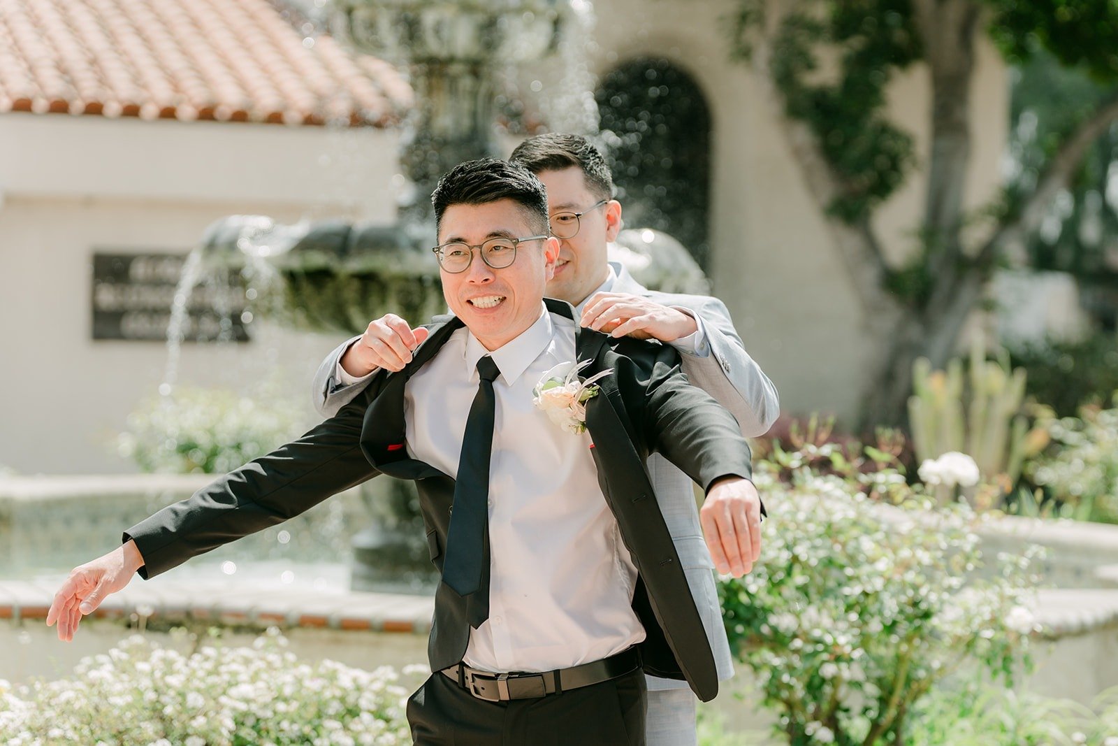 A groomsman hops onto Eric's back by the fountain