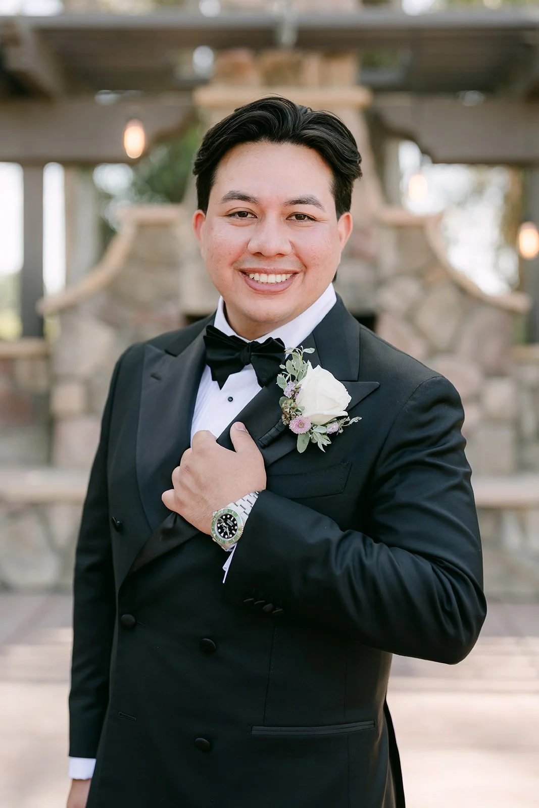 David checking his watch in a black tuxedo with a white boutonniere