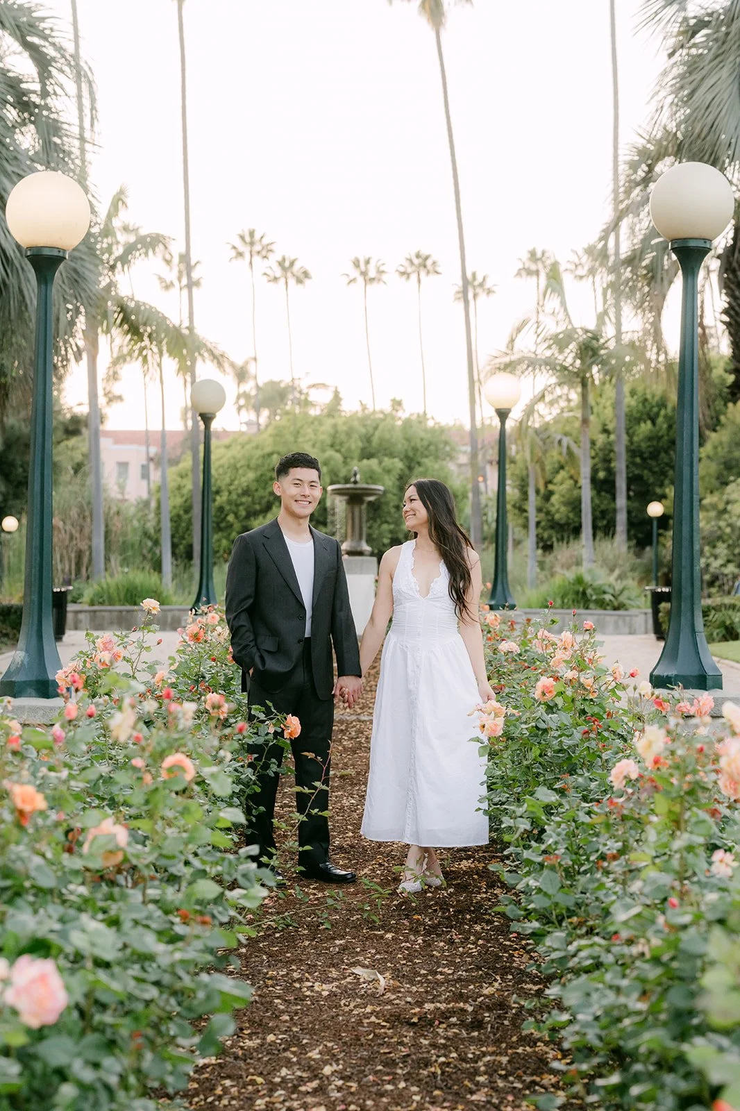 Jadee and Richard stand at the end of a path lined with roses.