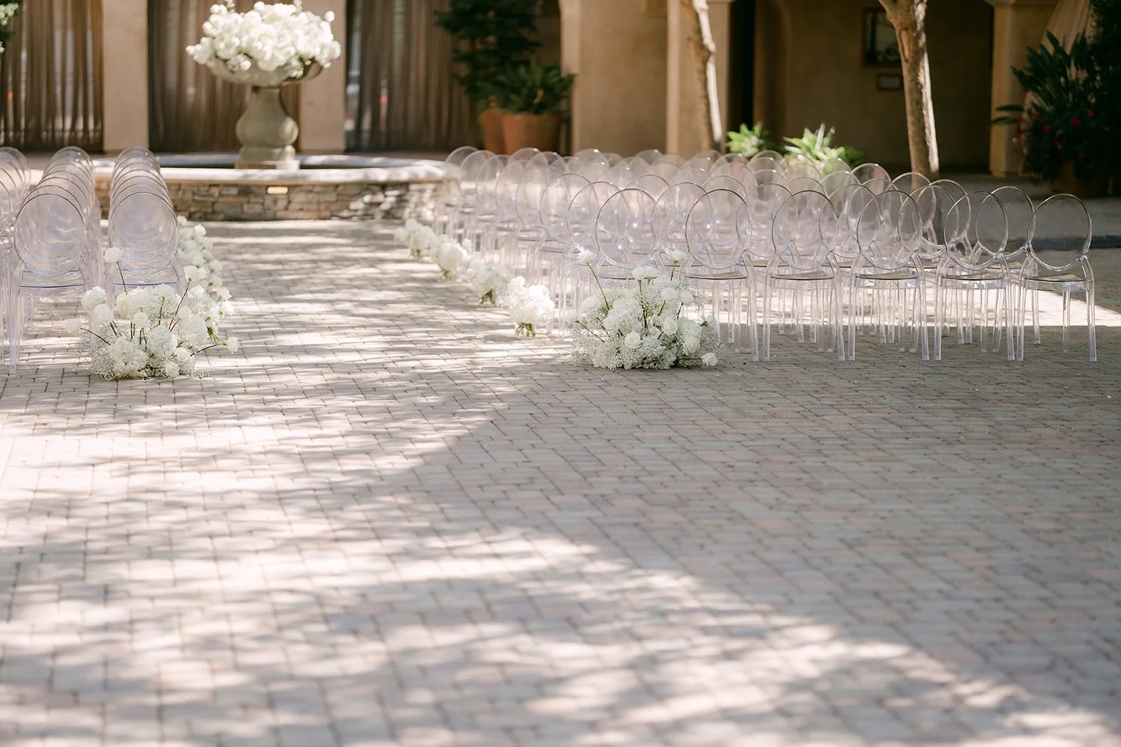 Aisle of ghost chairs and white florals leading toward the arches