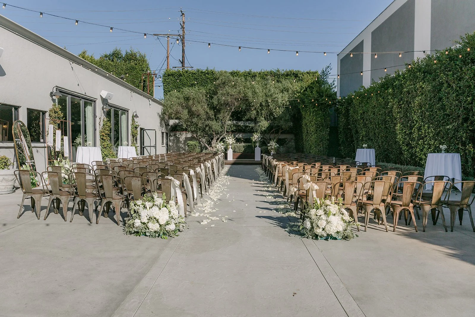 Wide view of the outdoor ceremony aisle with wooden chairs and white florals