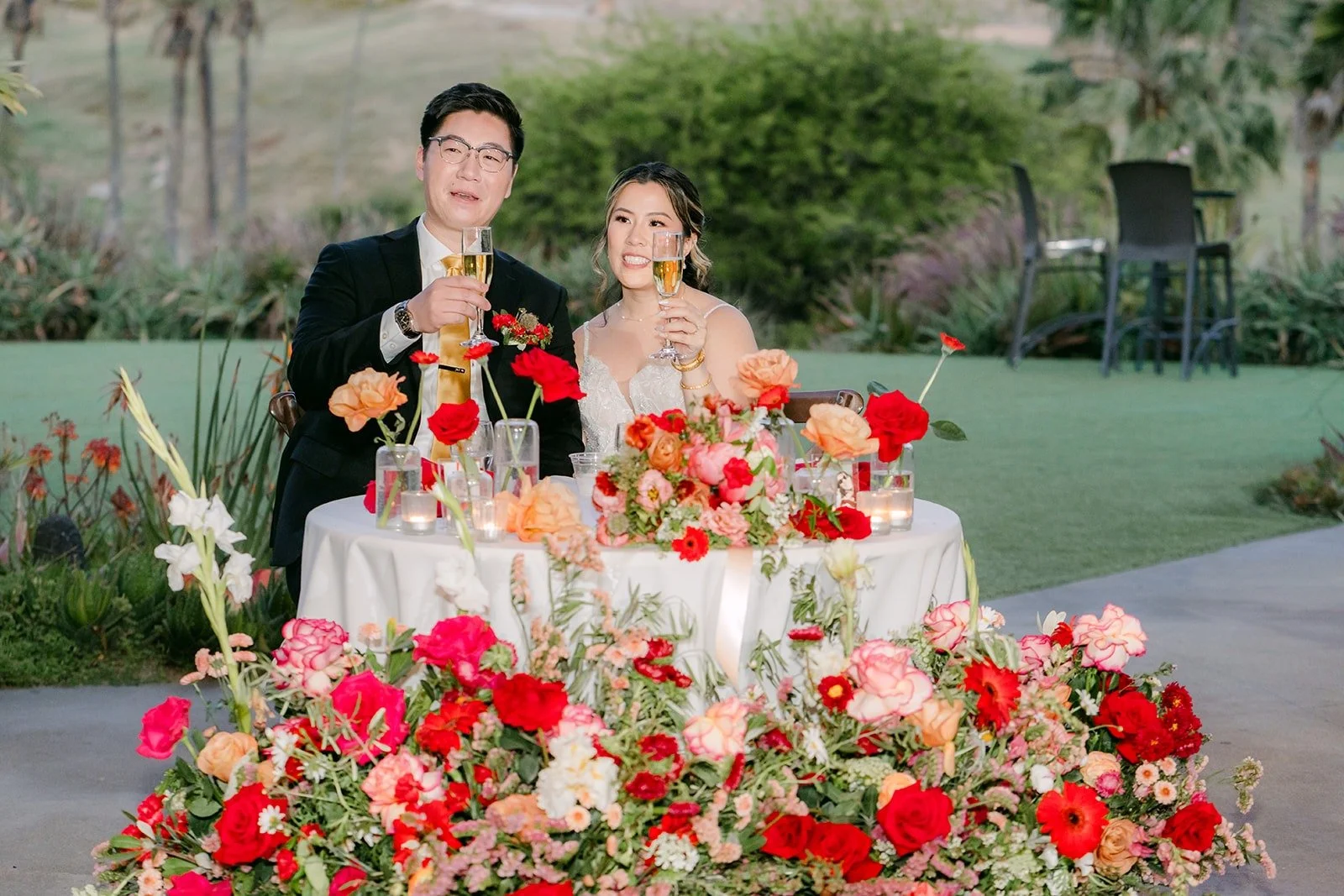 Joanne and Zach laughing at their sweetheart table full of red and pink flowers