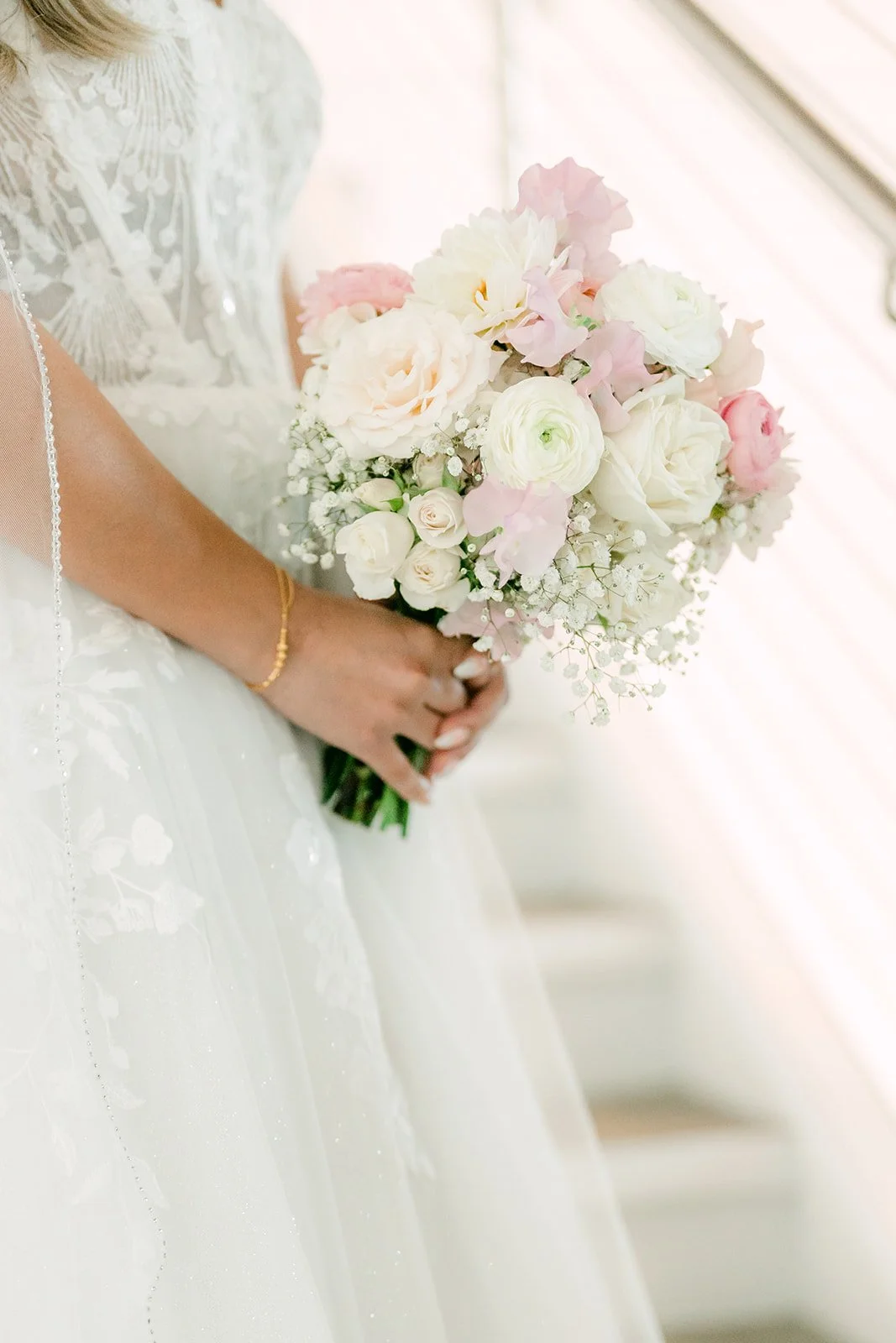Bridal bouquet of blush roses and ivory blooms held against a lace gown