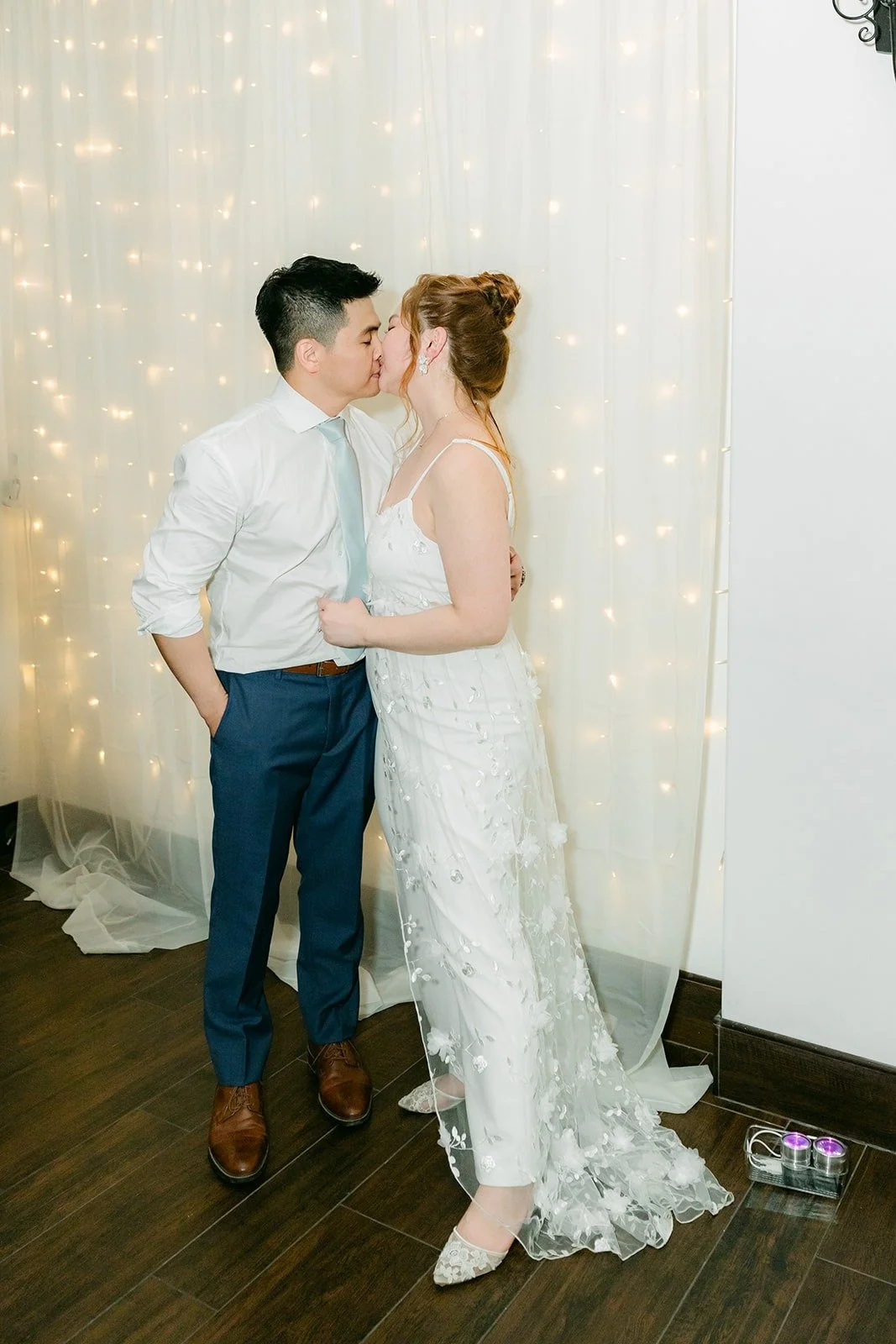 Jerrick kissing Joanna in front of the string light backdrop in the parlor
