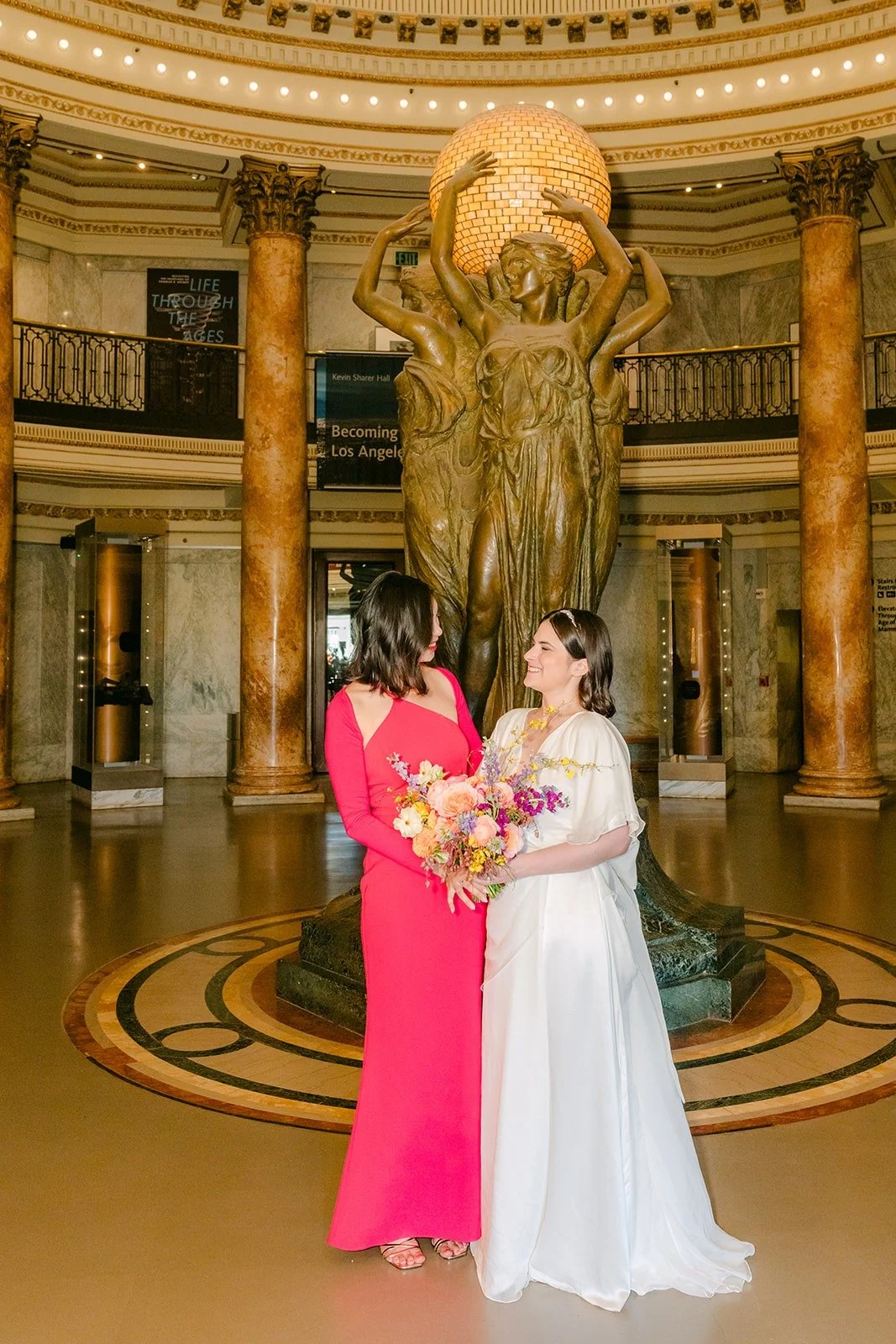 Jessie and a bridesmaid in hot pink sharing a laugh in the Rotunda