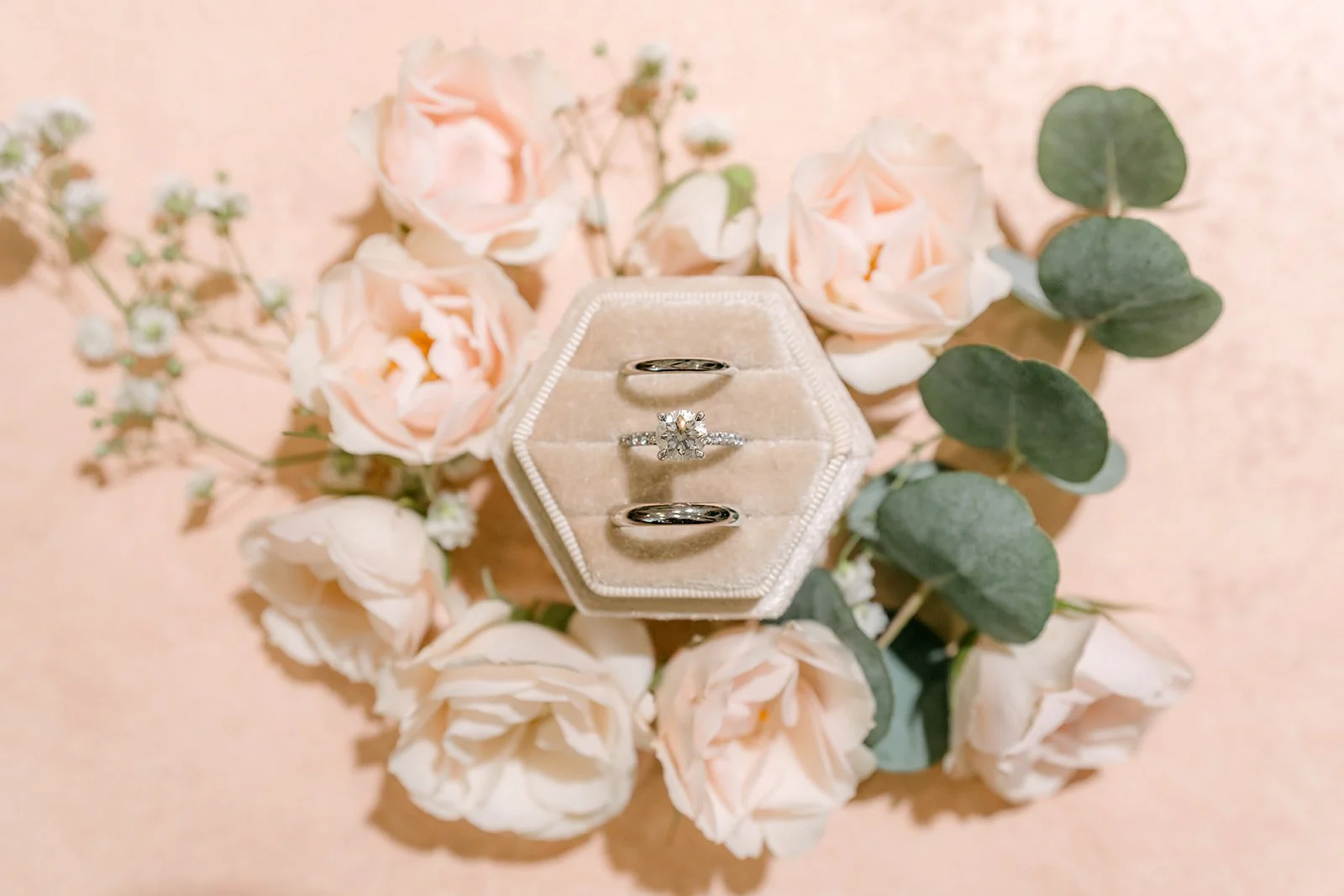 Wedding rings in a hexagon ring box surrounded by blush roses and eucalyptus