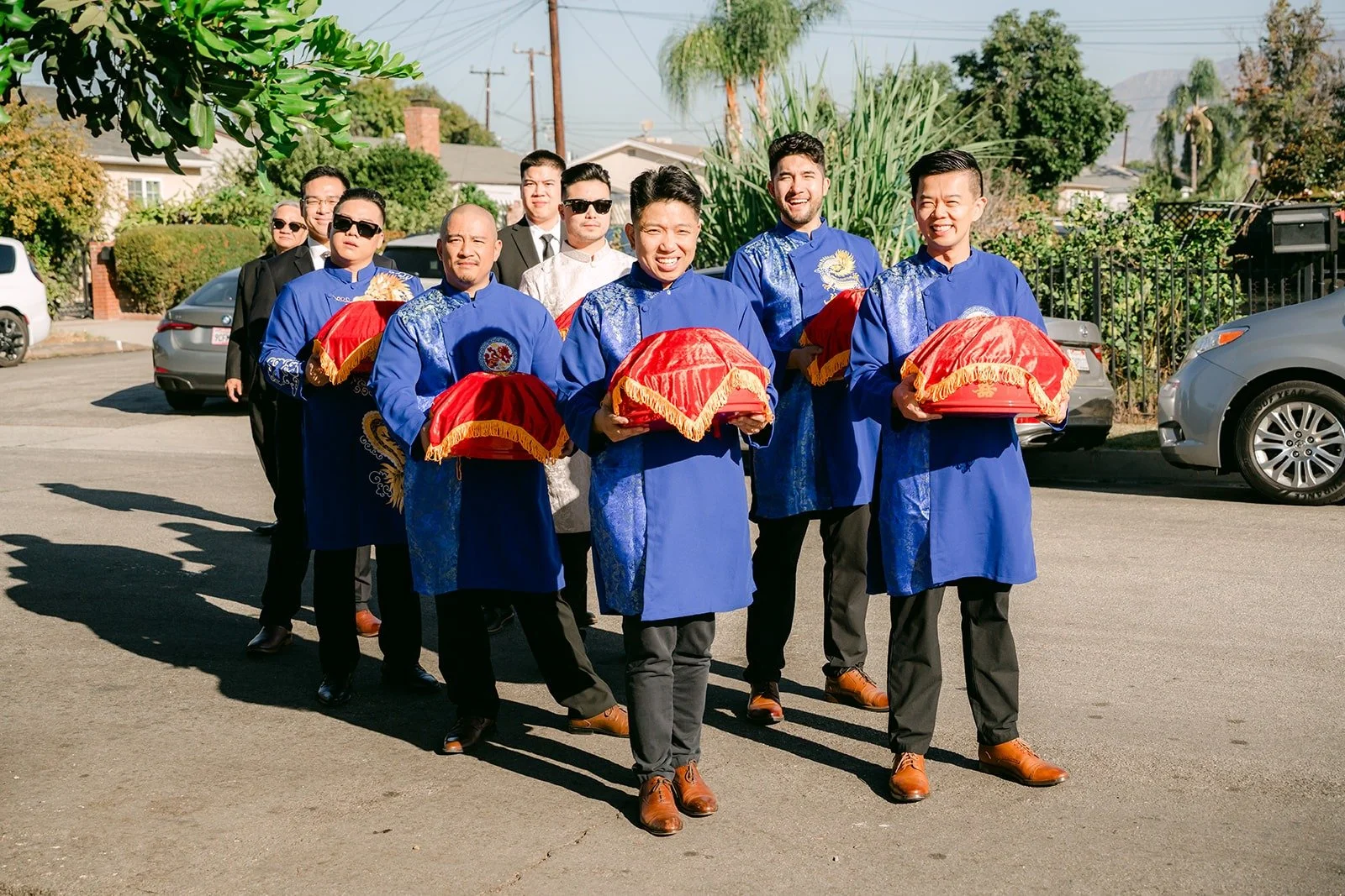 Kevin's groomsmen in blue ao dai walk down the street carrying red gift boxes for the procession