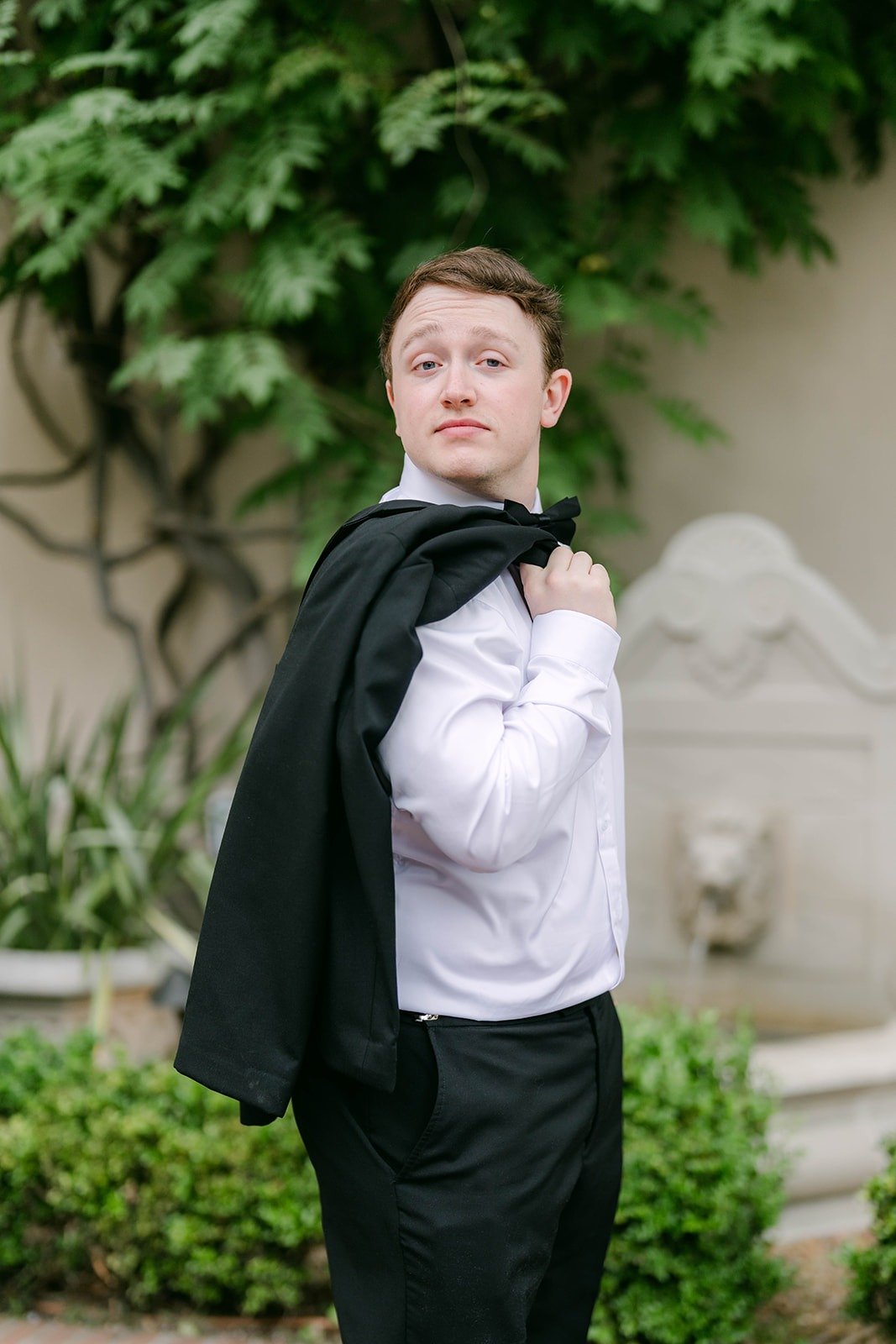 Matthew with his tuxedo jacket over his shoulder in front of green vines