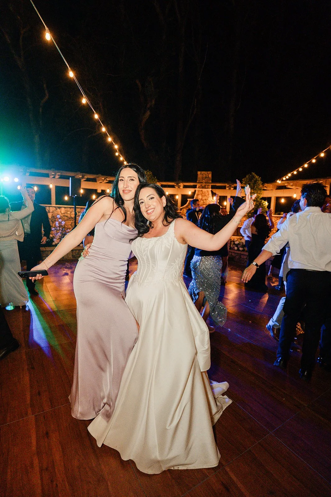 Bride dancing with friends under string lights