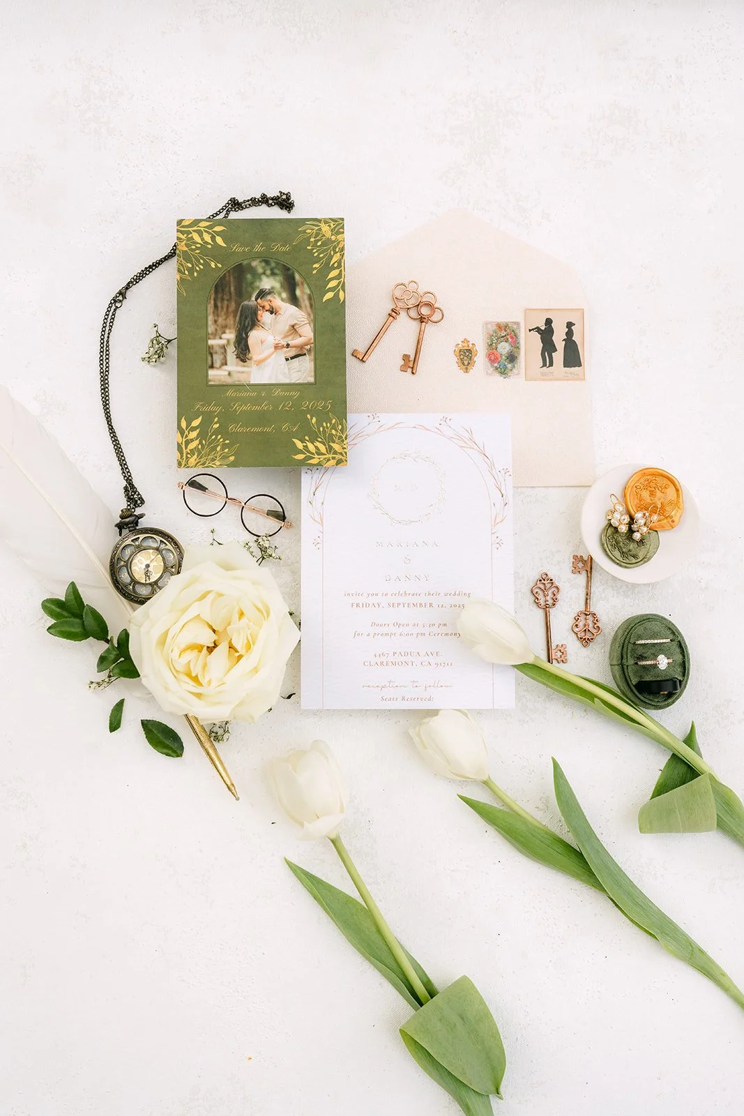Flat lay with the invitation, an engagement photo, vintage keys, a pocket watch and white tulips